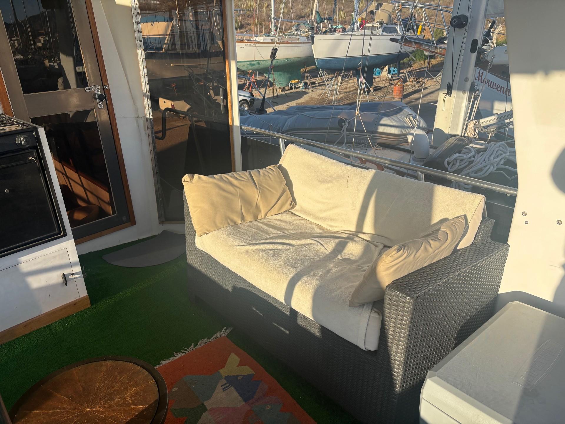 Cozy outdoor seating on a boat with a wicker sofa, colorful rug, and marina view.
