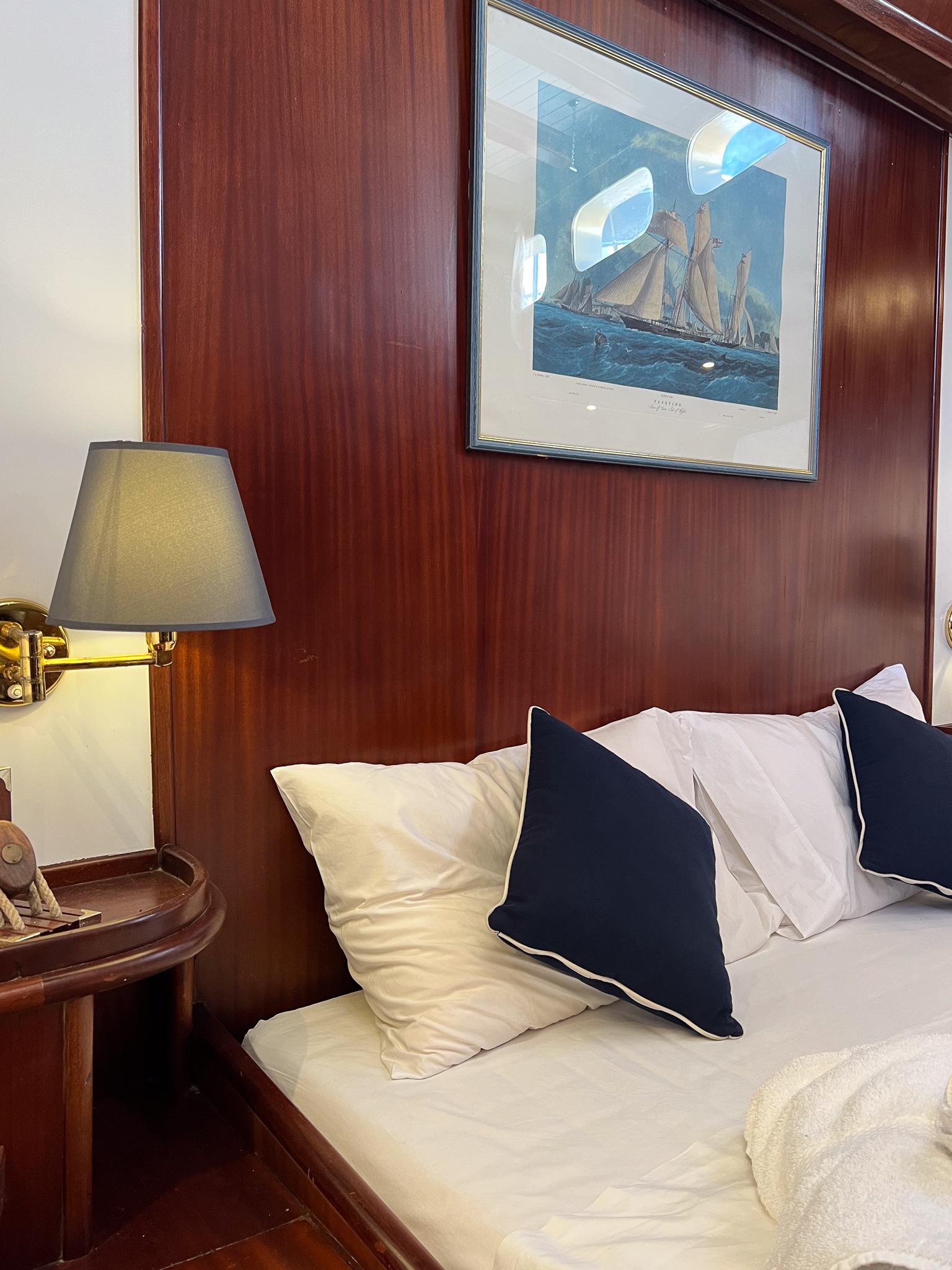 Cozy ship cabin with wooden paneling, nautical artwork, and elegant bedding, Psarros Shipyard 1969.