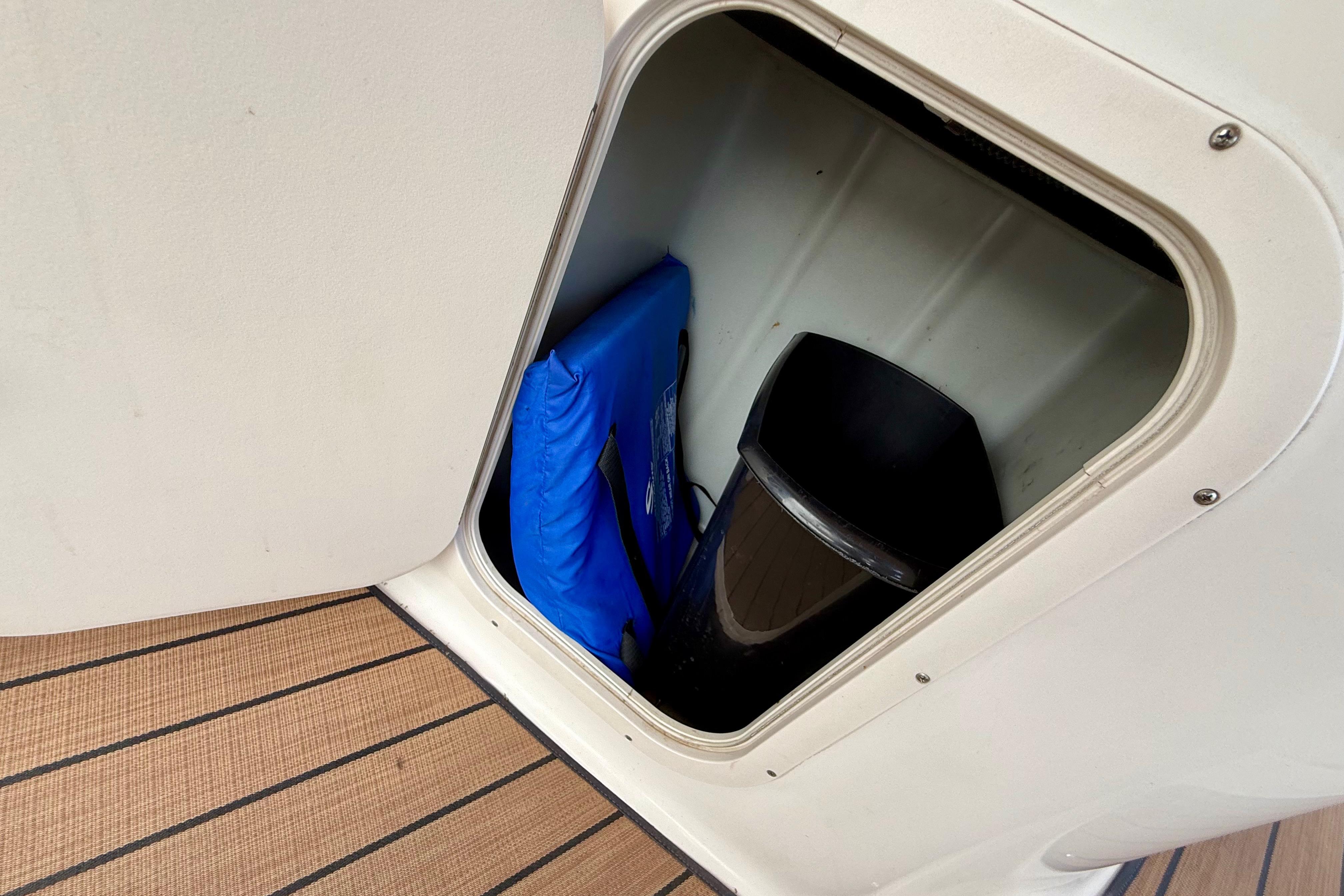 Storage compartment on 1999 Chaparral Signature 300 boat with blue cushion and black container.