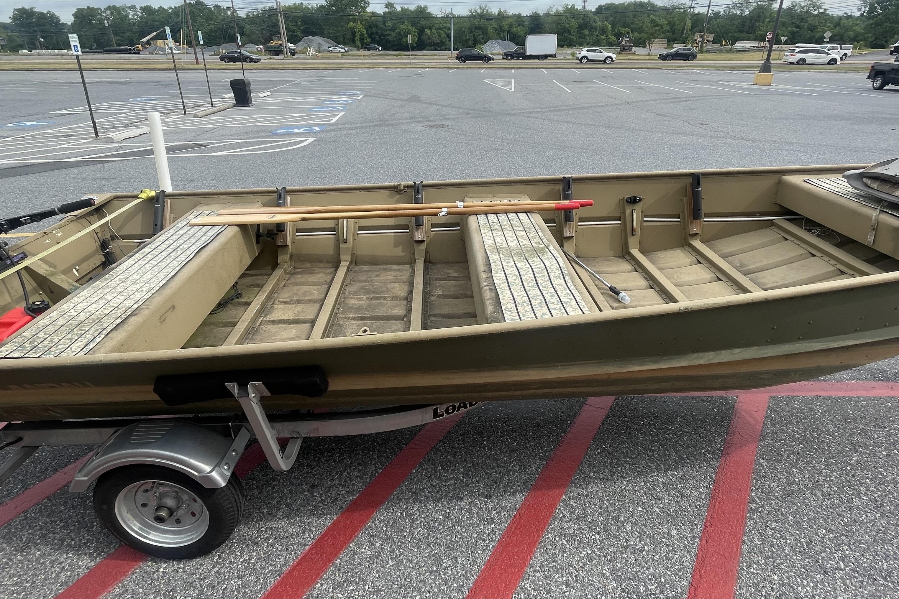 1986 Landau 1664 Jon boat on trailer in parking lot, showcasing interior seating and storage.