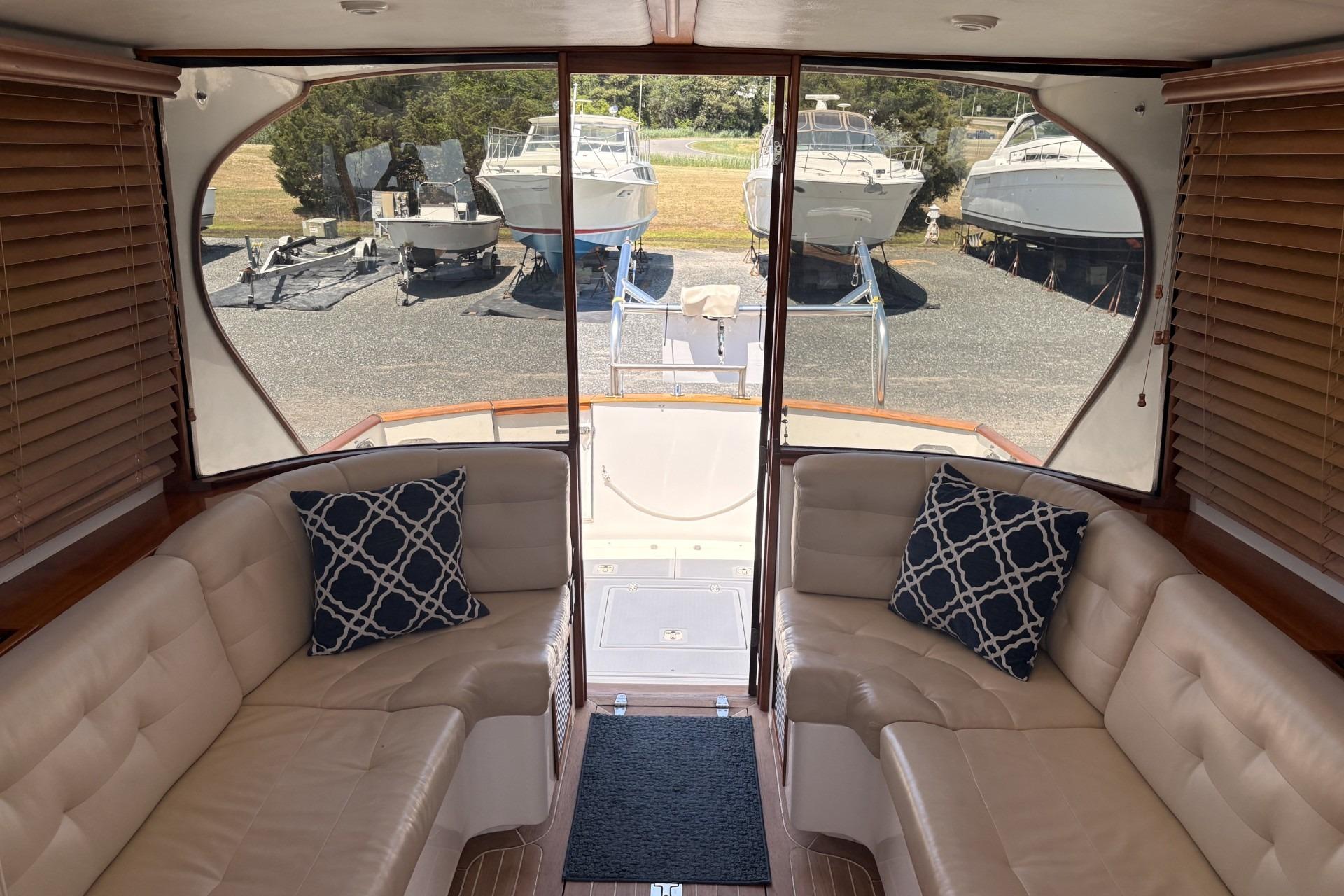 Luxurious boat interior with beige seating, patterned cushions, and a view of docked boats outside.