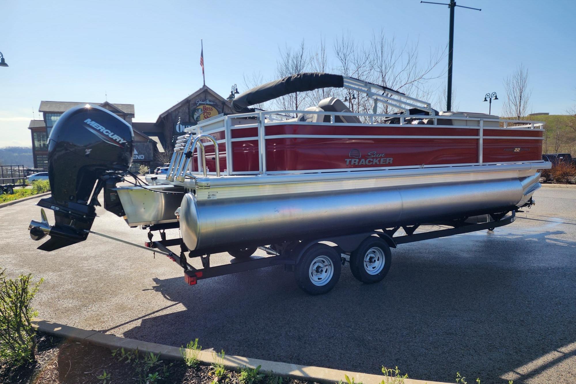 2026 Sun Tracker Fishin' Barge 22 DLX pontoon boat on trailer, parked outdoors.