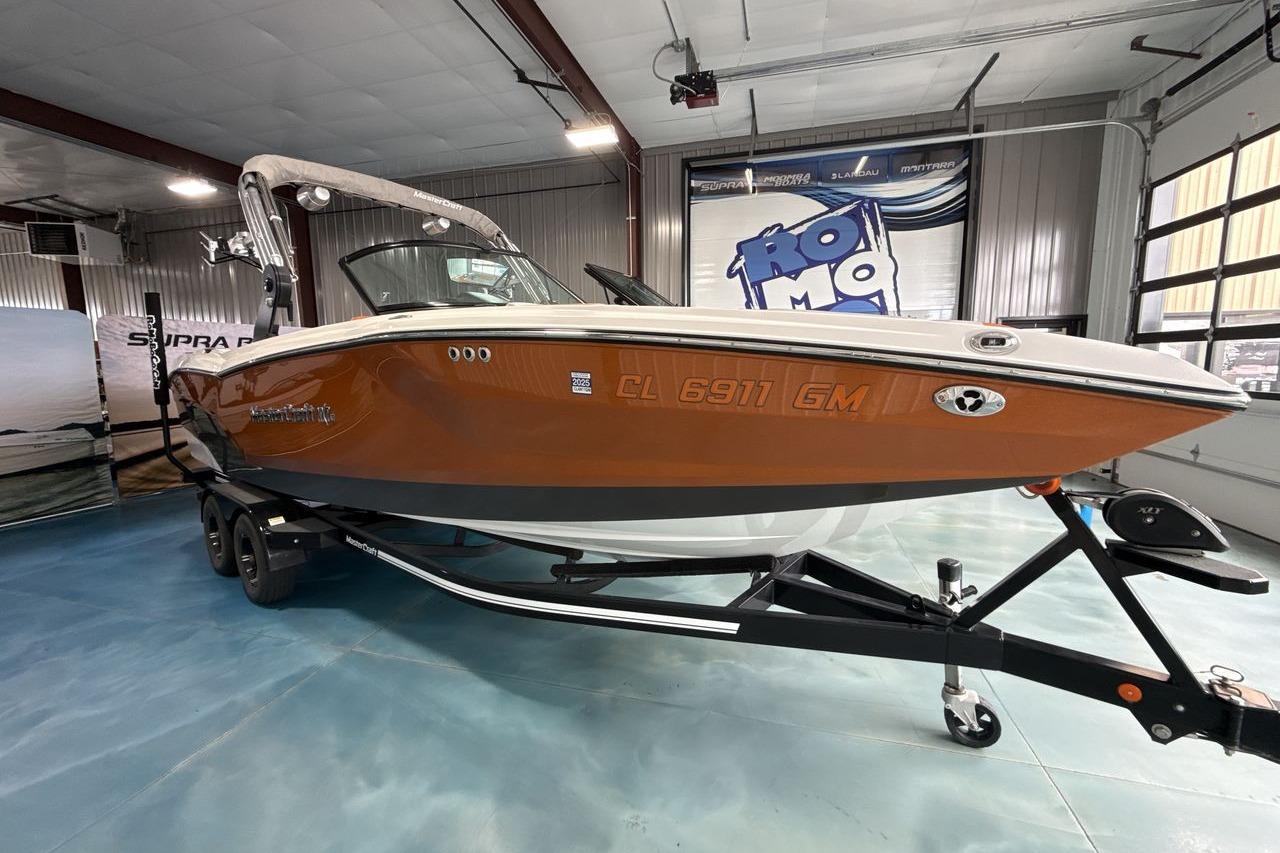 2021 MasterCraft NXT24 boat in showroom, orange hull, on trailer.