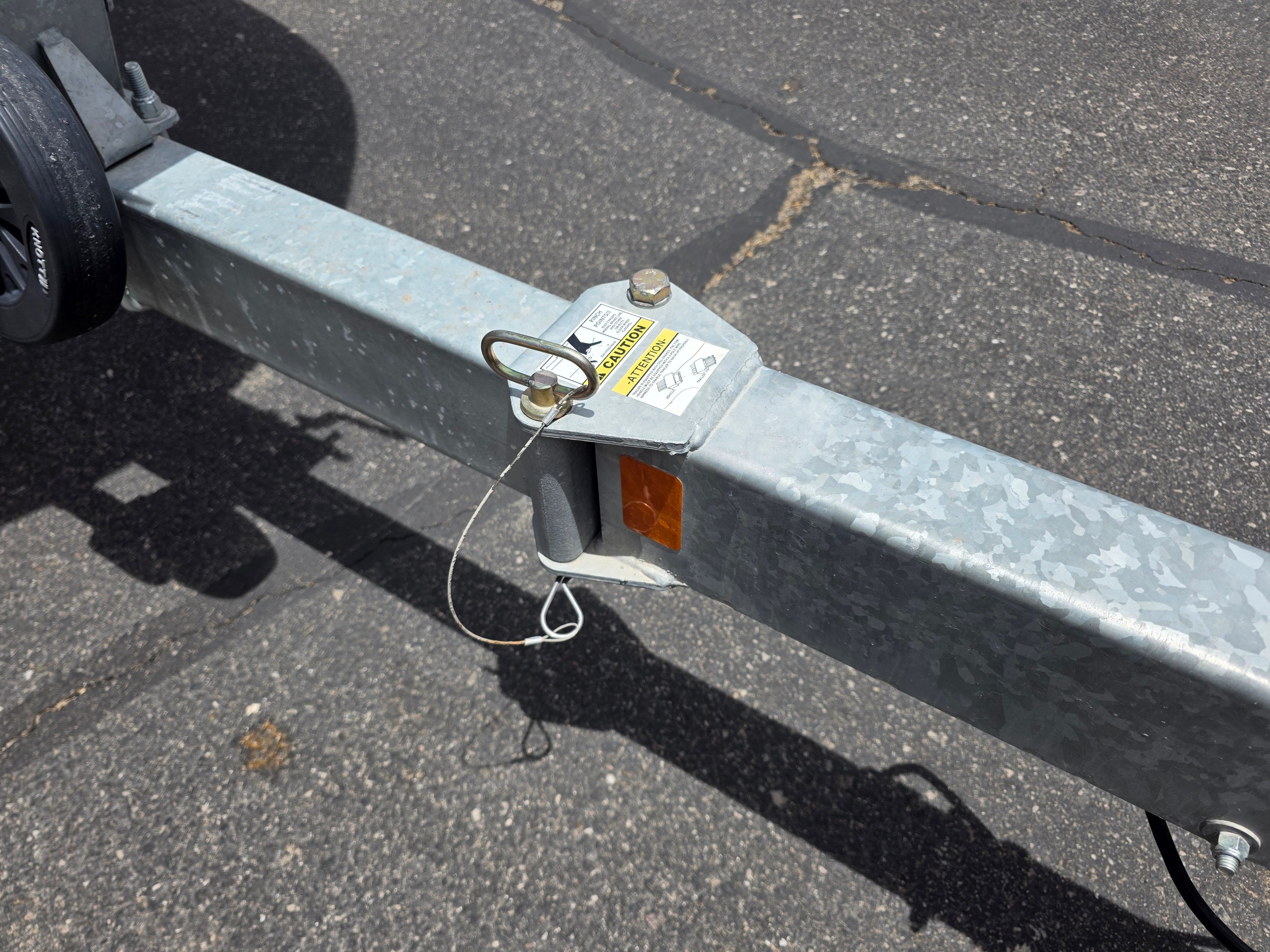Close-up of a boat trailer with safety lock and cable on asphalt.