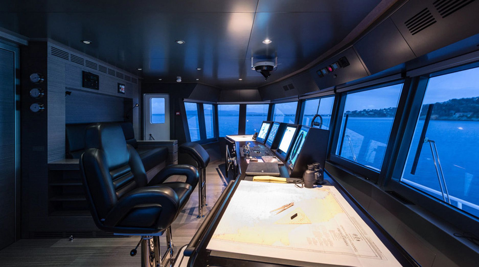The image shows a yacht's helm with modern navigation systems and large windows overlooking the sea.