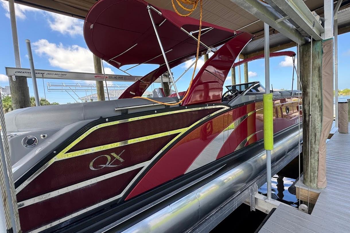 2024 Bennington QX27 pontoon boat docked, featuring sleek red design and modern canopy.
