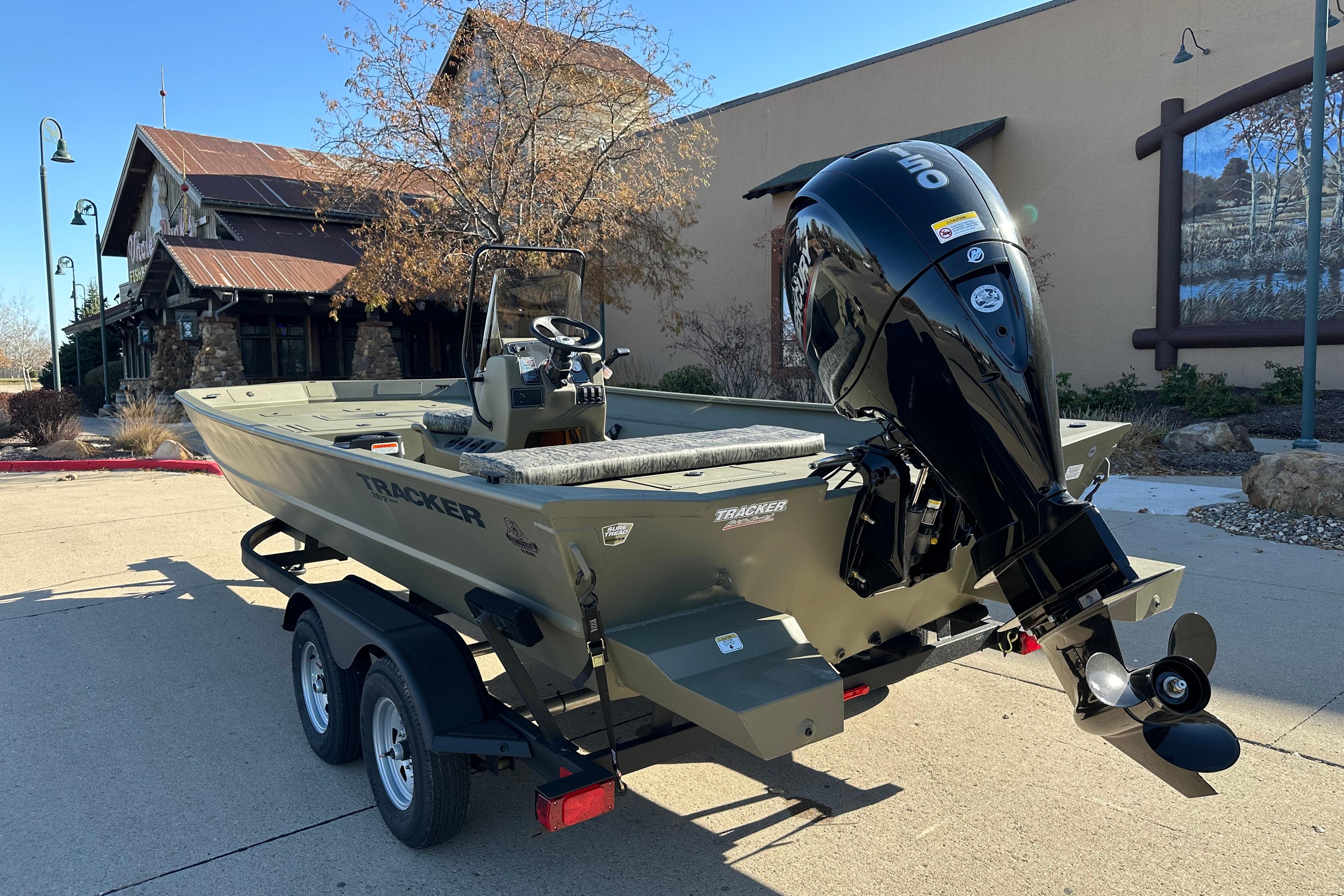 2026 Tracker Grizzly 2072 CC boat on trailer, parked outdoors near rustic building.