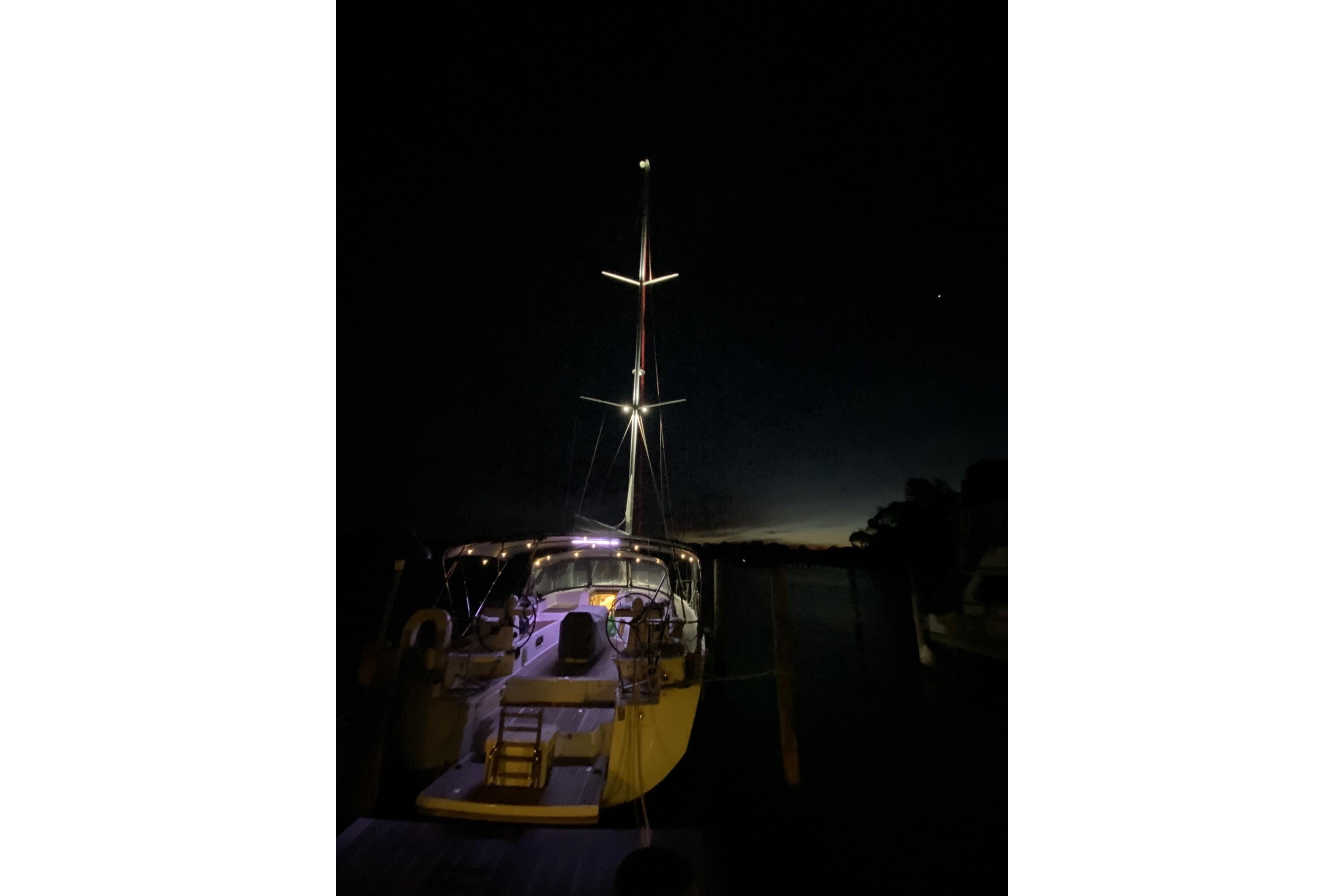 2018 Jeanneau 51 sailboat illuminated at night, docked with a dark sky backdrop.