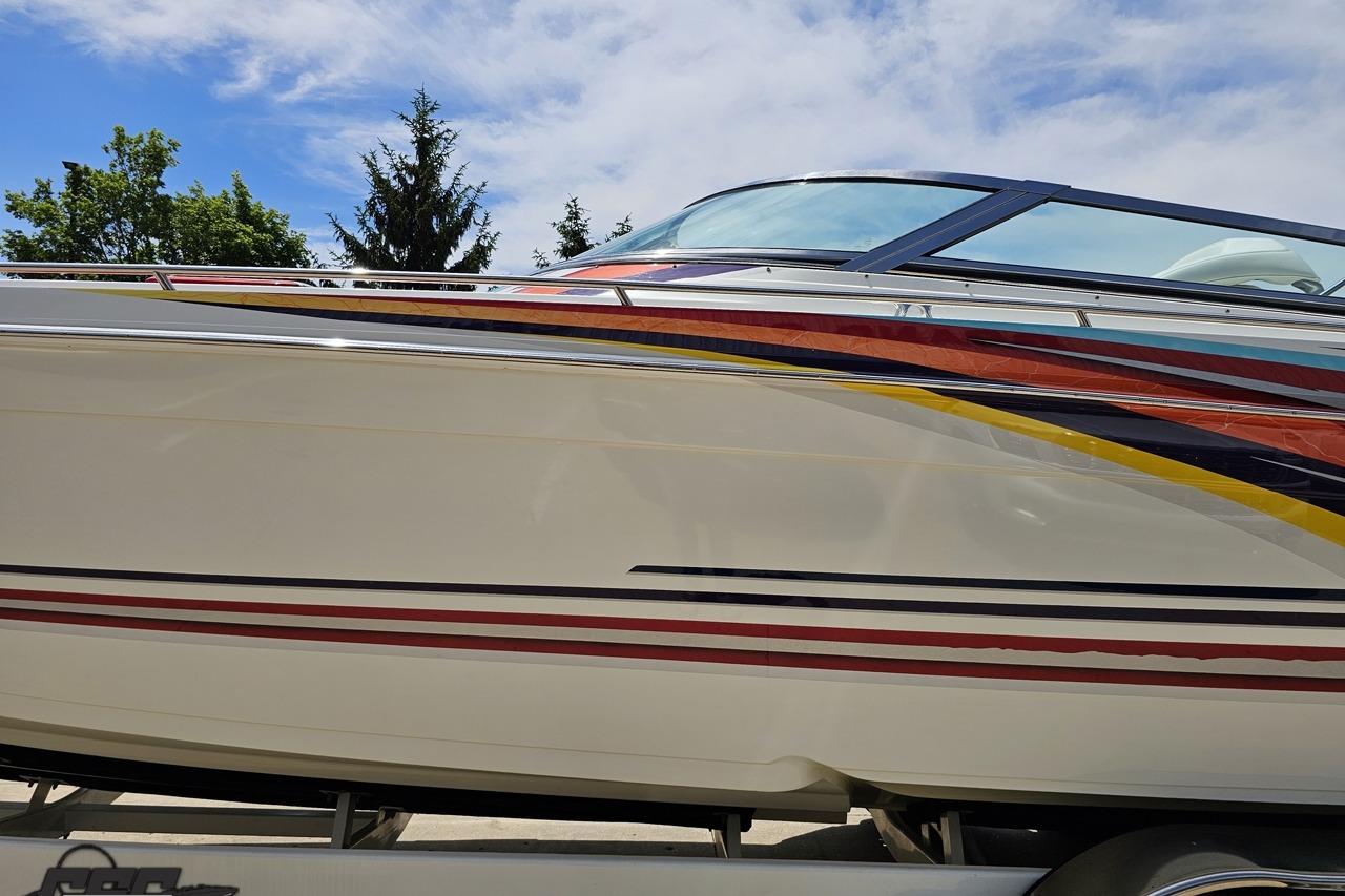 2002 Formula 382 FASTech boat with colorful stripes, parked on a trailer under a blue sky.