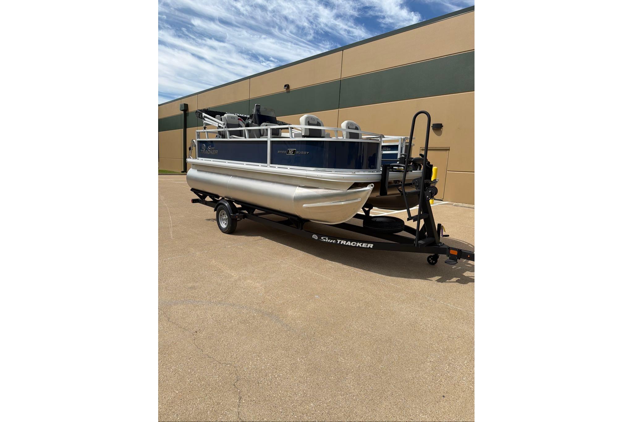 2026 Sun Tracker Bass Buggy 16 XL Select pontoon boat on trailer, parked outdoors.