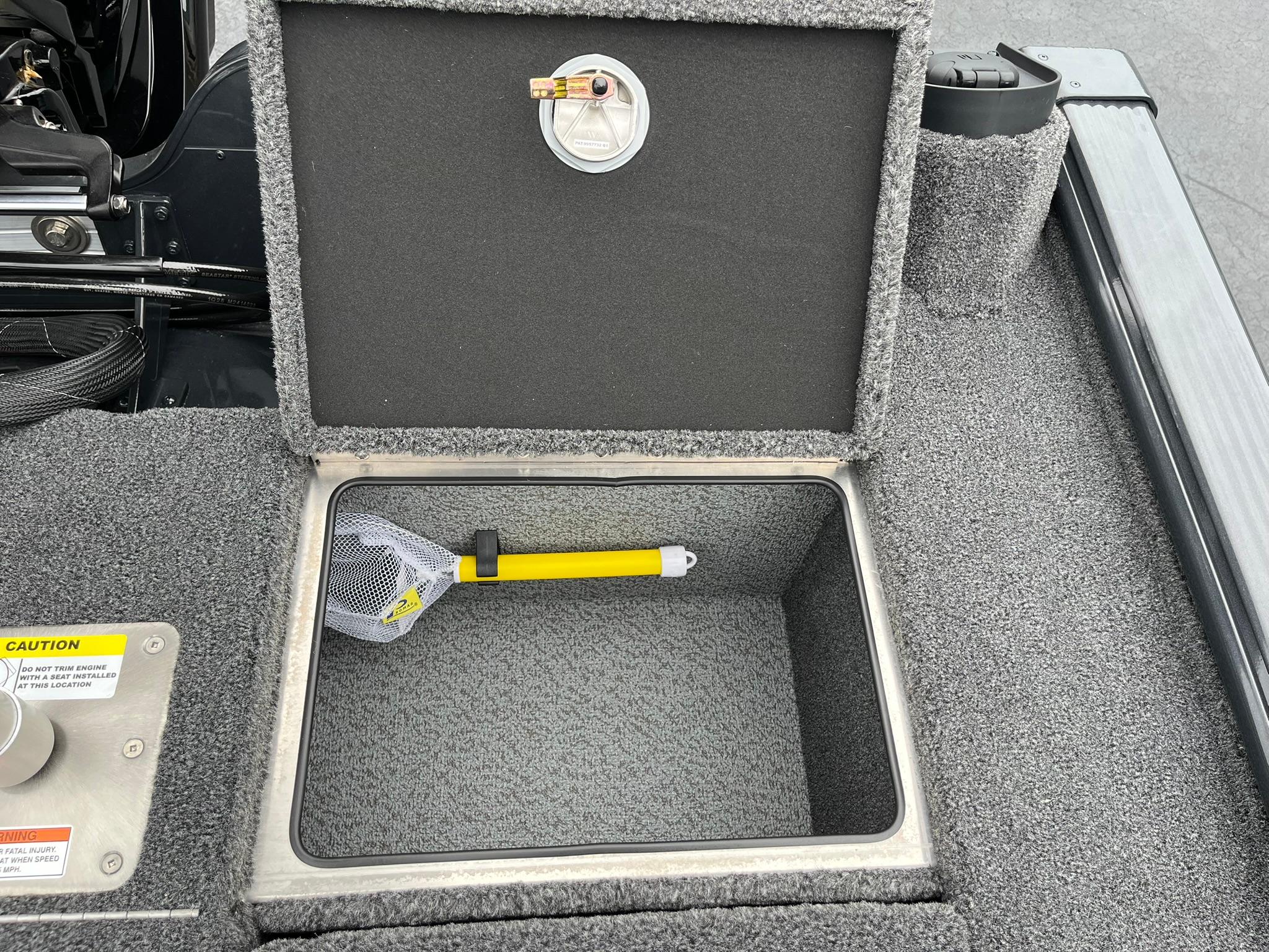 Open storage compartment in 2026 Lund 1875 Pro-V Bass XS boat with a yellow-handled net.