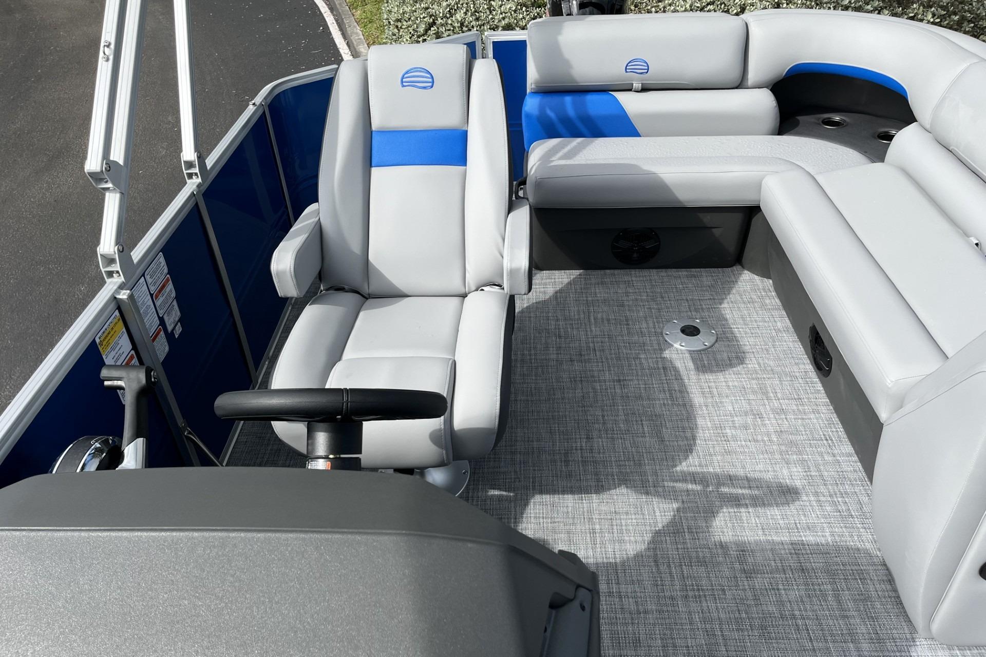 2026 Sun Tracker Party Barge 20 DLX interior with gray and blue seating, steering wheel, and carpeted floor.