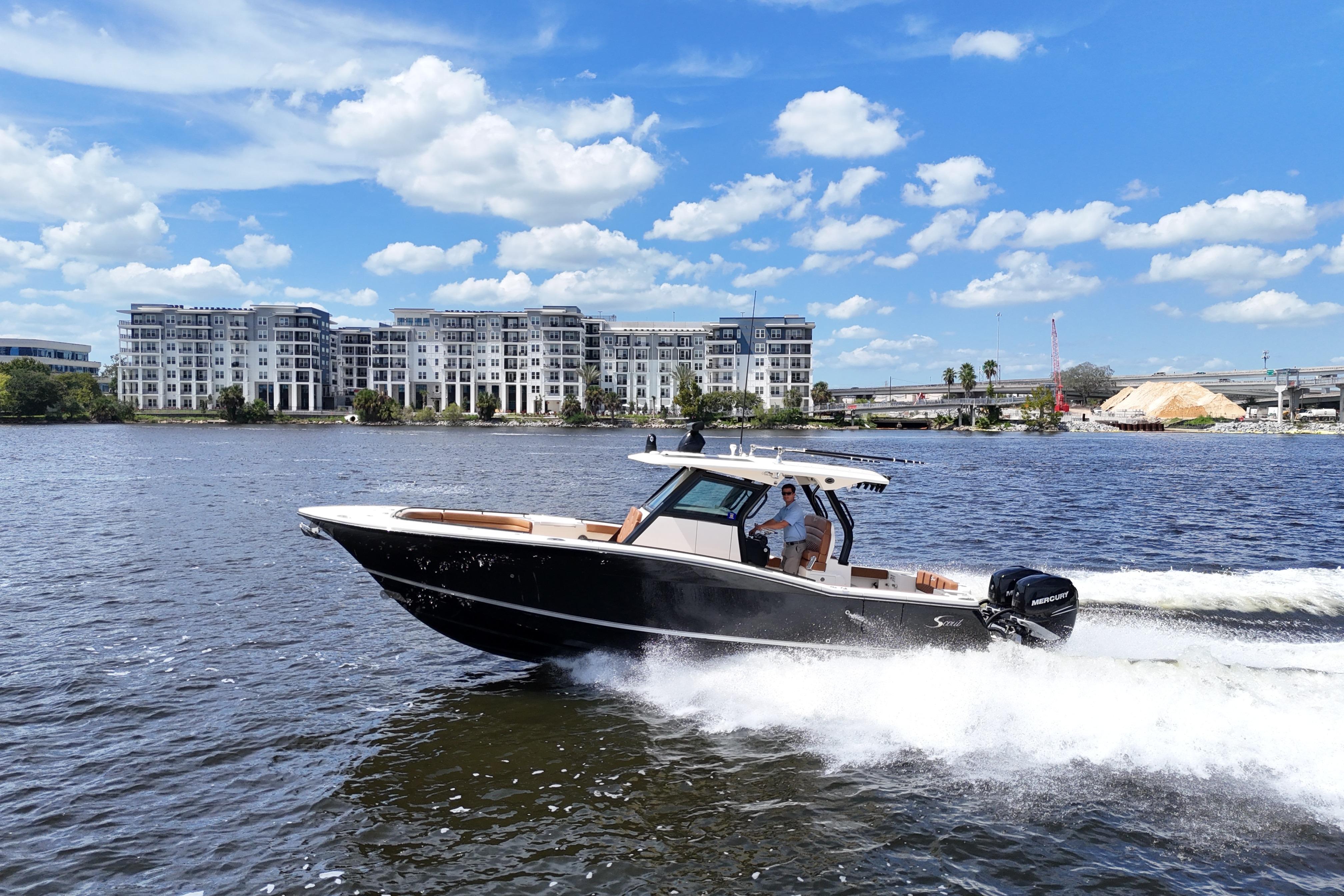2021 Scout 330 LXF boat cruising on a river with modern buildings in the background.