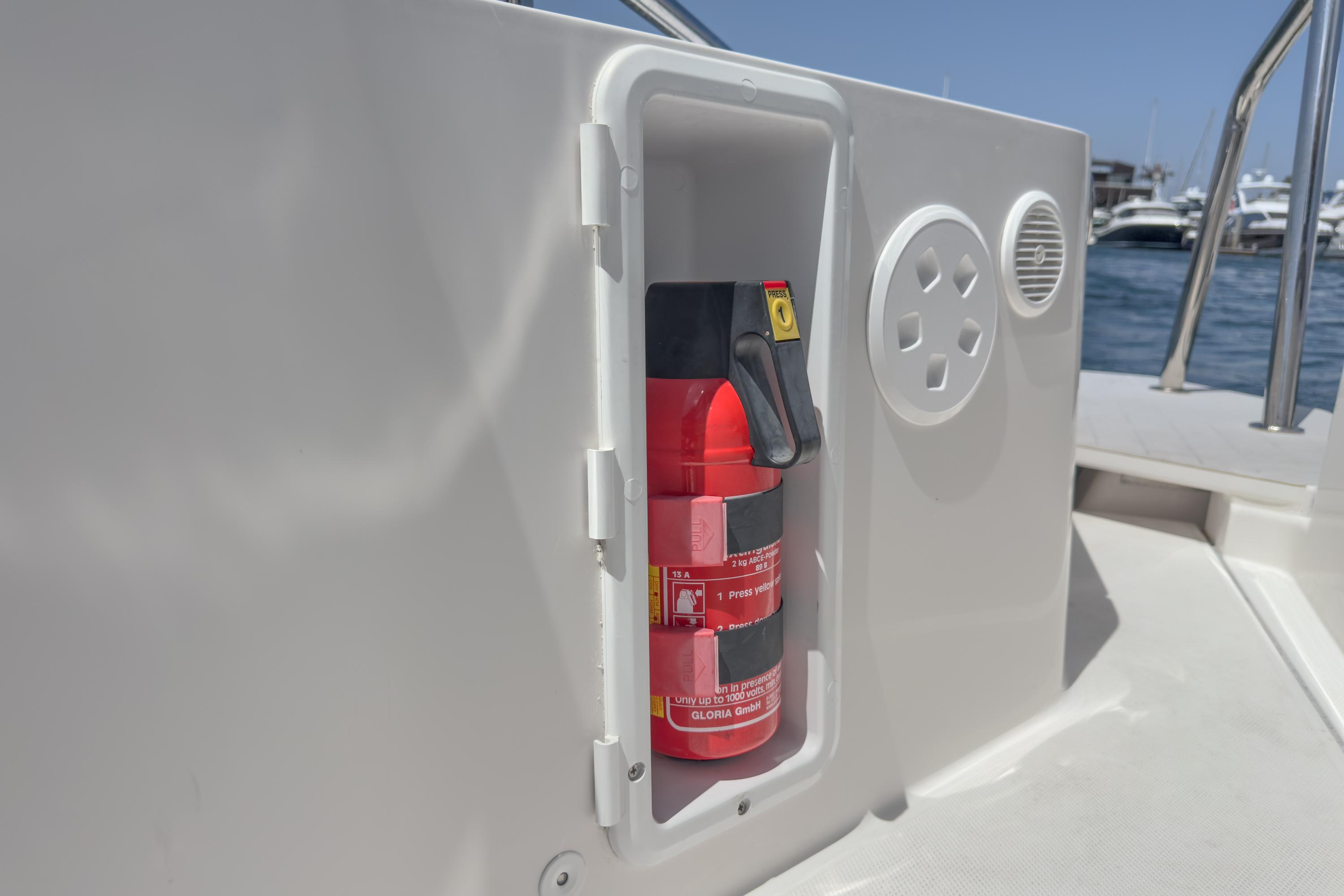 Fire extinguisher in compartment on 2019 Axopar 28 CABIN boat, docked by the water.