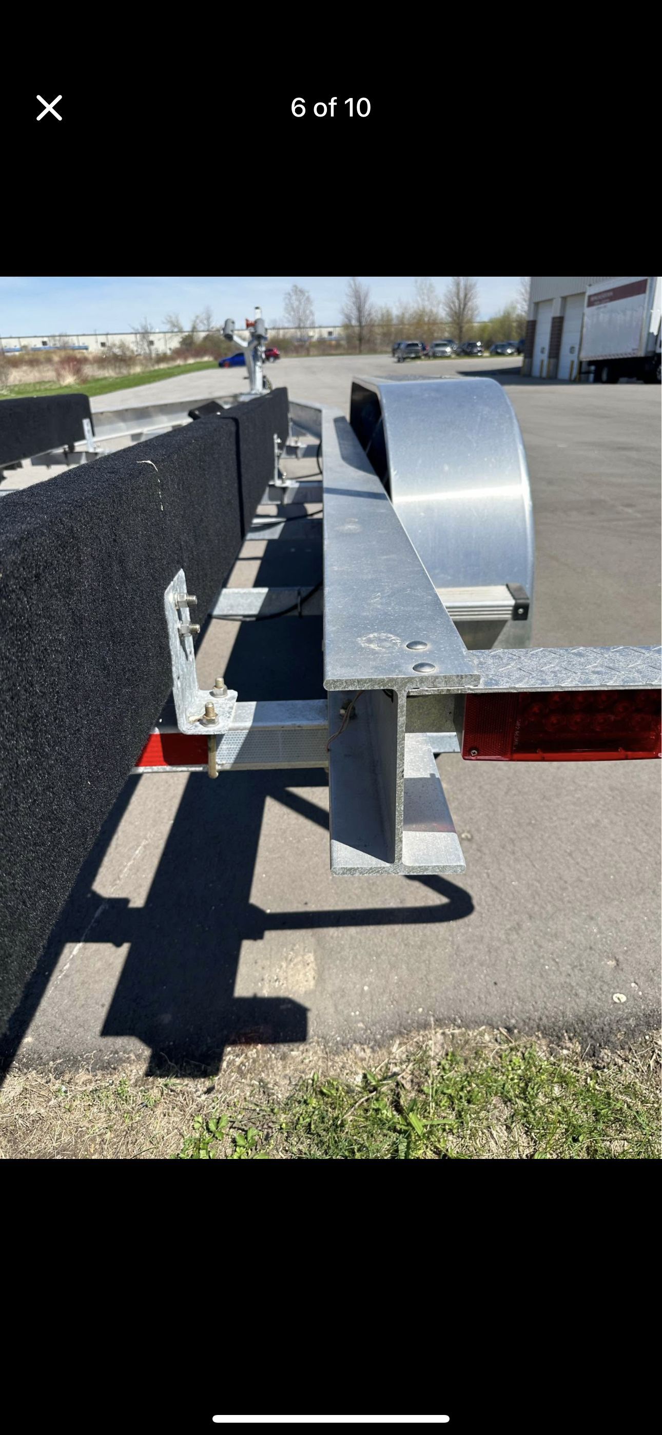 A boat trailer with a metal frame and black padding is parked on a lot.