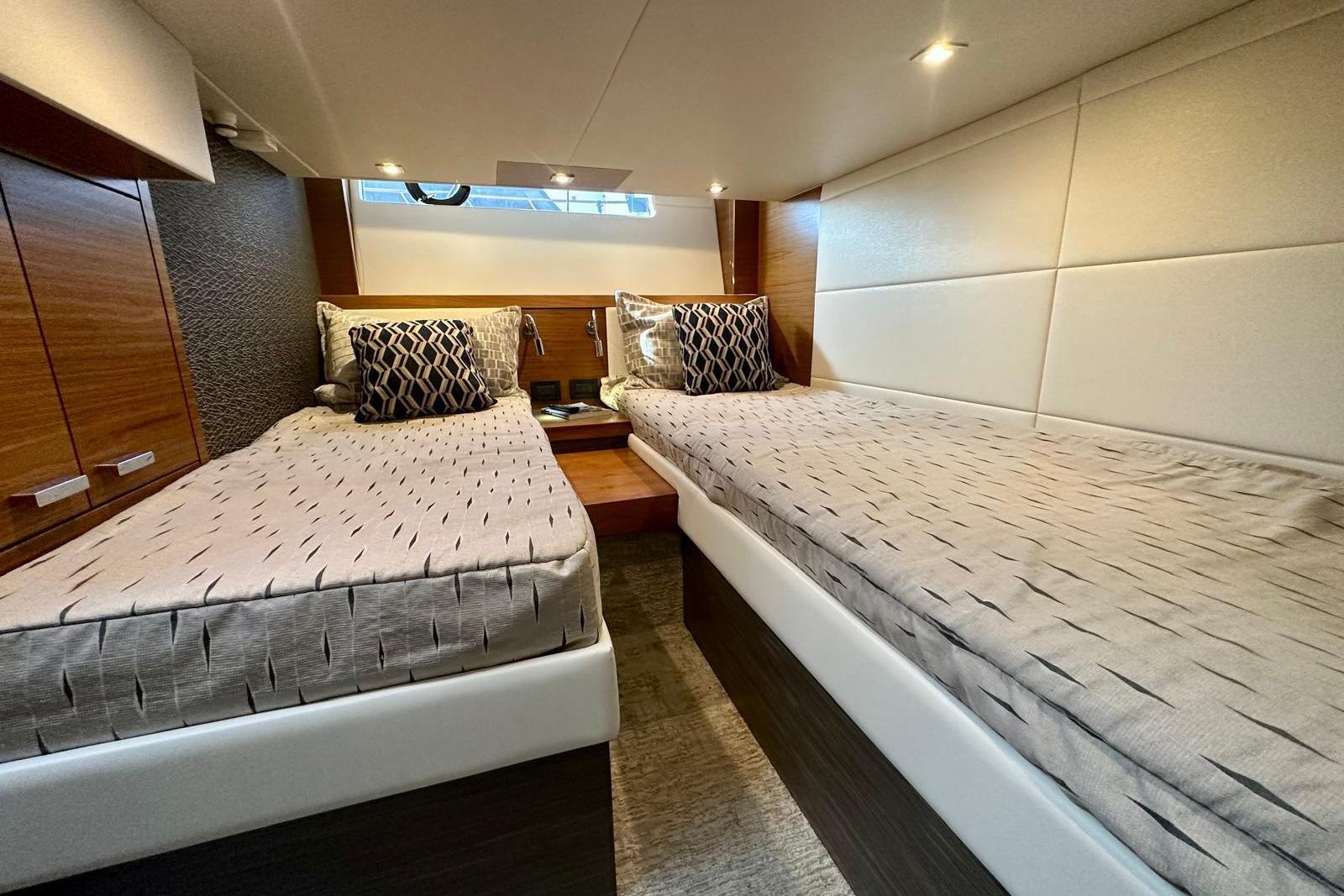 Luxurious twin cabin interior of 2019 Tiara Yachts F44 Flybridge, featuring elegant bedding and lighting.