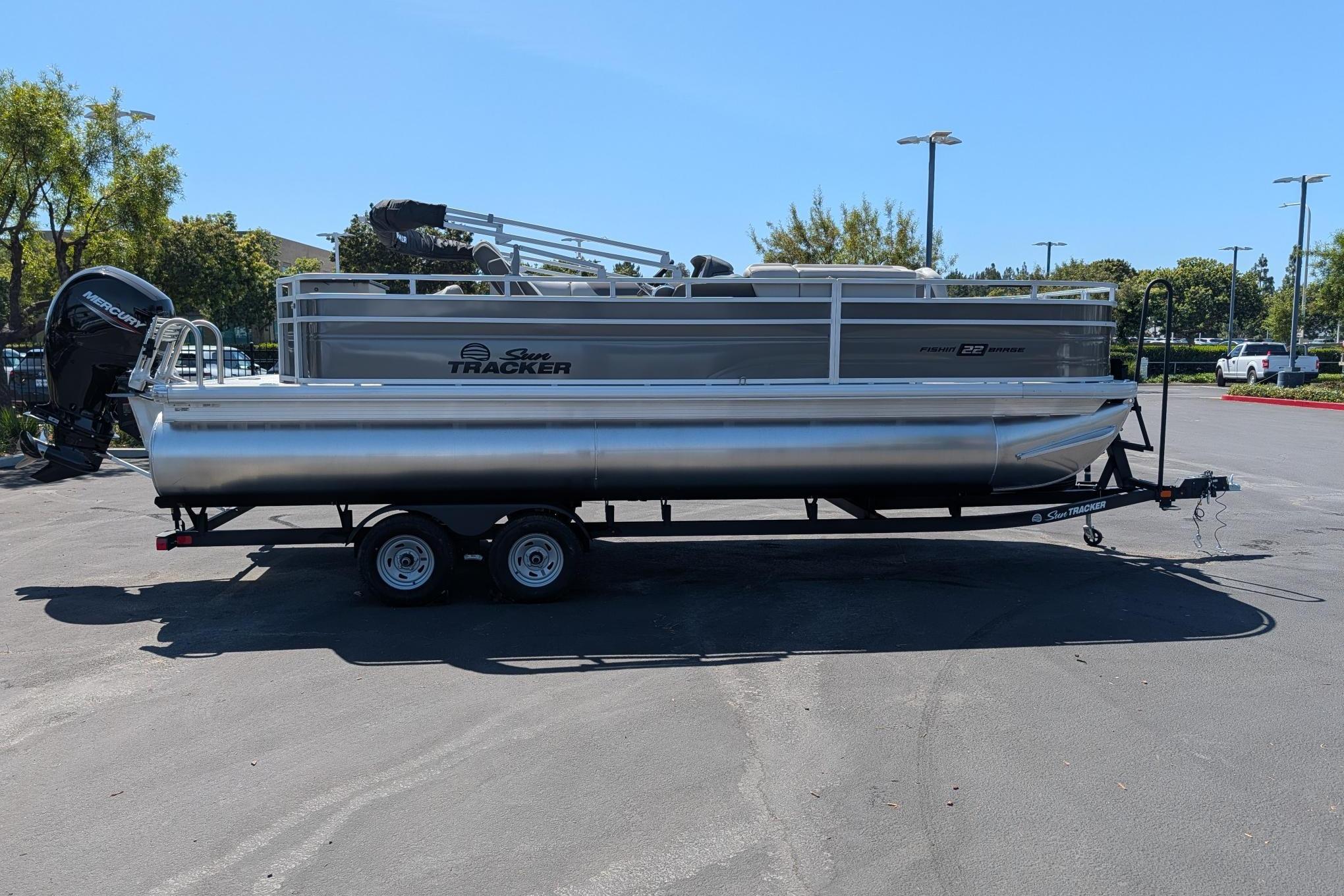 2026 Sun Tracker Fishin' Barge 22 DLX pontoon boat on trailer in parking lot.