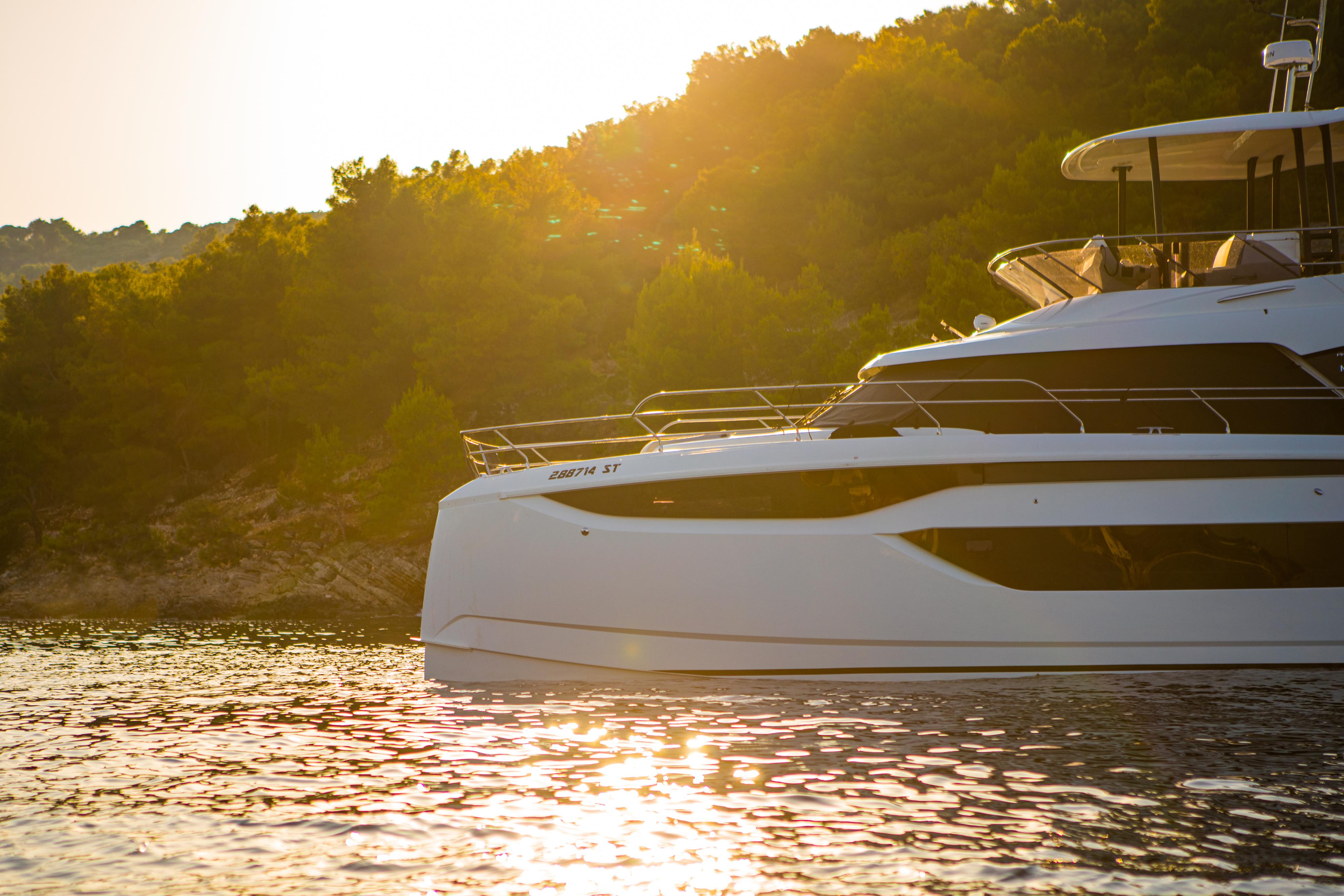 Luxurious 2024 Prestige M48 yacht cruising at sunset near a forested shoreline.