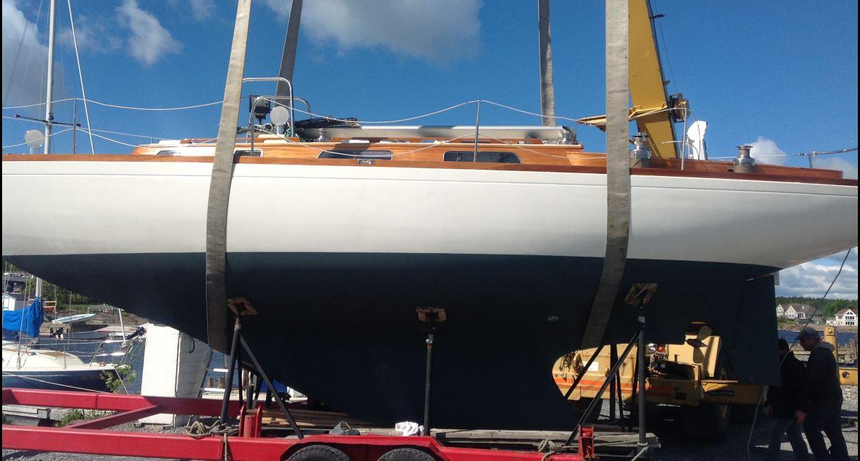 1973 Ohlson 38 sailboat on trailer, blue hull, wooden deck, under clear sky.