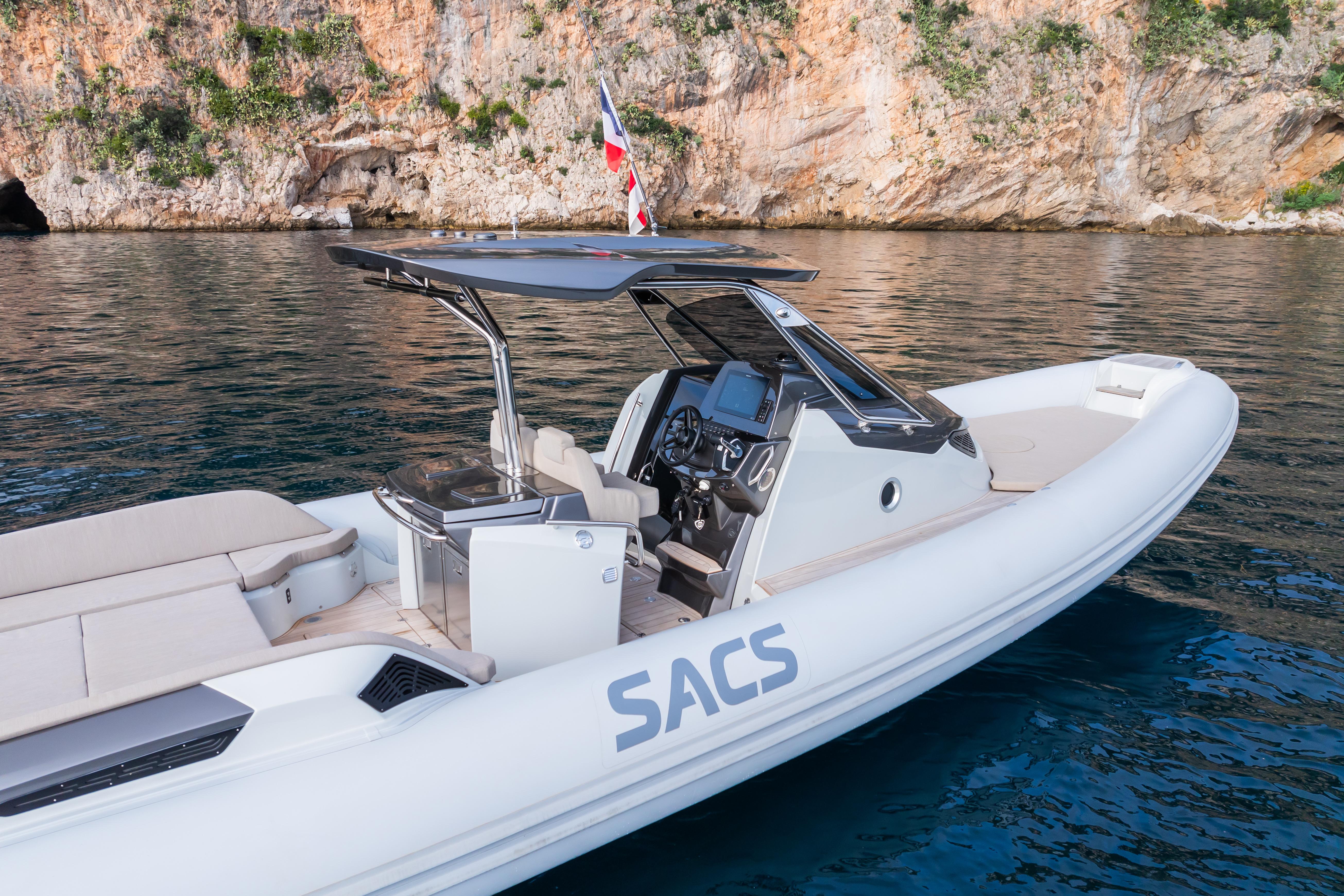 2025 SACS STRIDER 11 OPEN BACK boat on water near rocky shoreline.