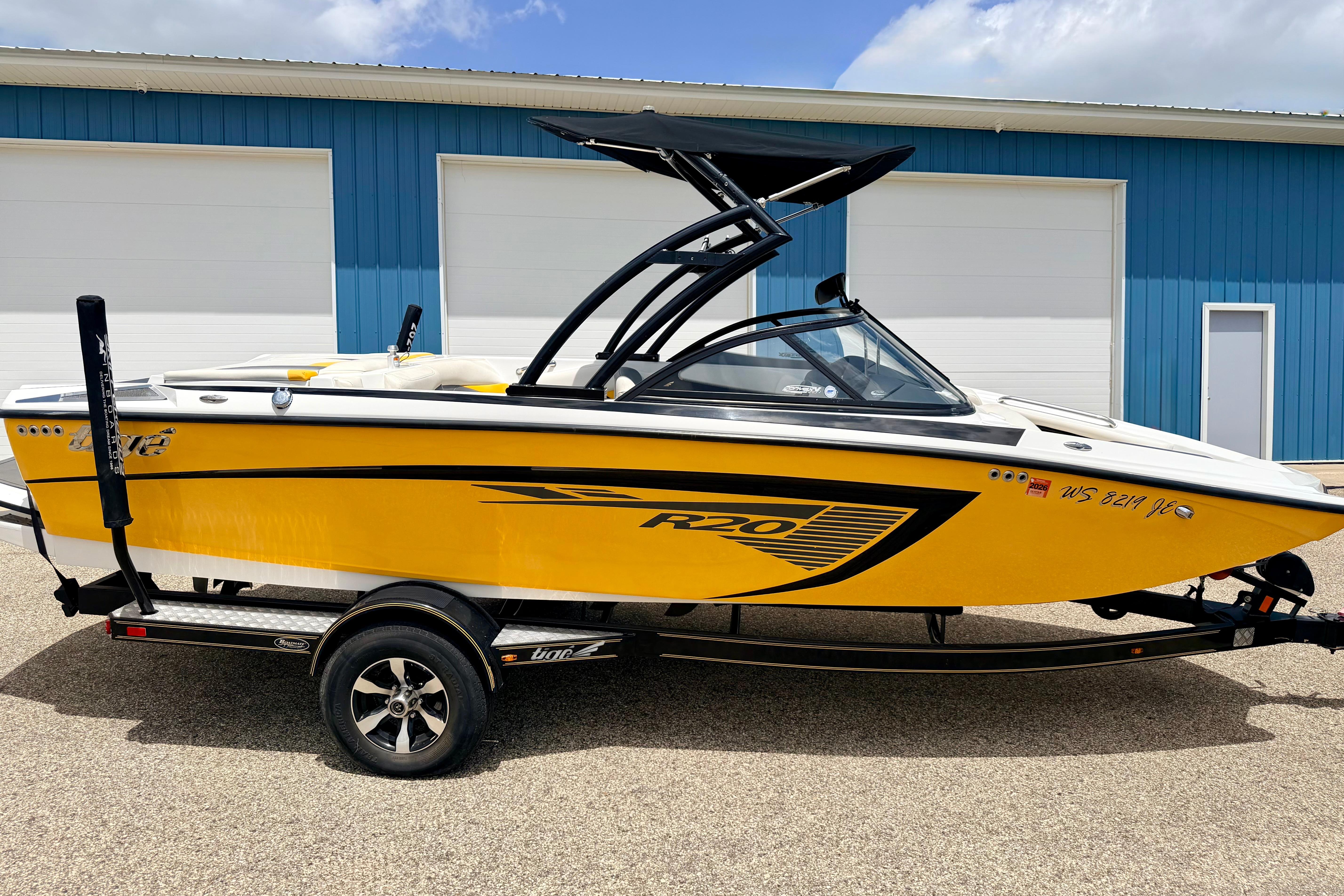 2014 Tigé R20 boat in vibrant yellow, parked on a trailer near a blue building.
