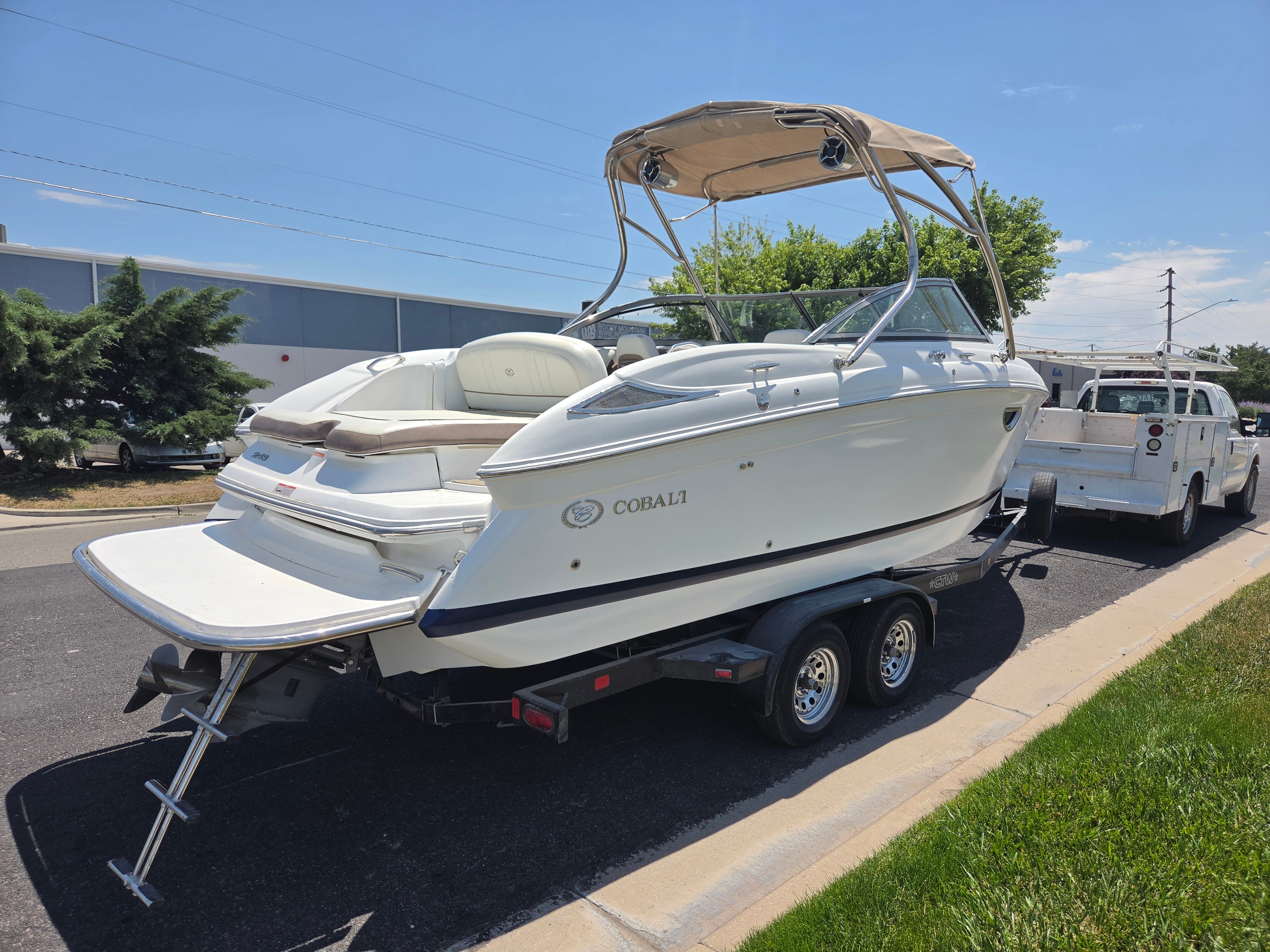 A Cobalt 243 boat on a trailer, parked on a street next to a white vehicle.