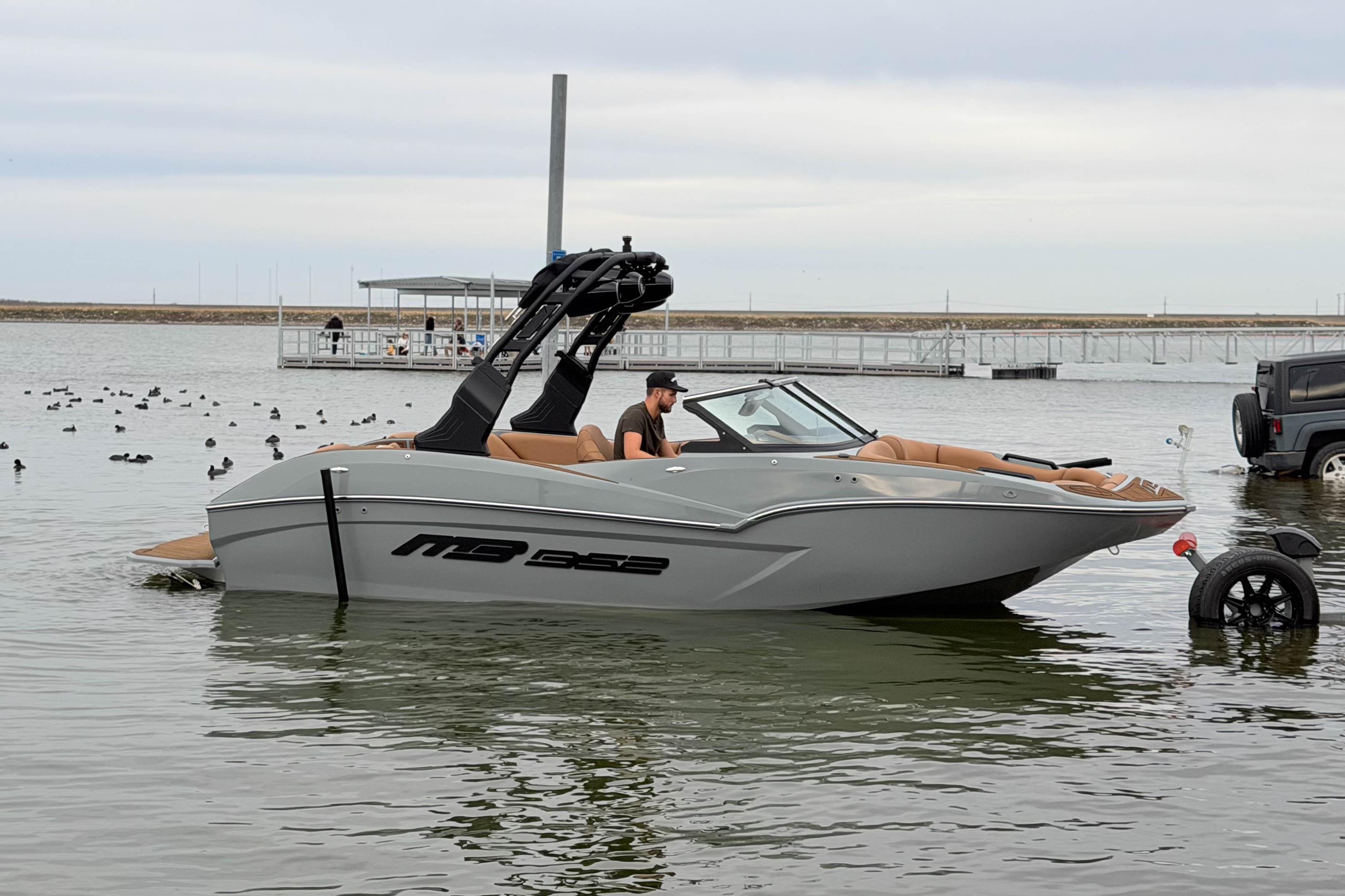 2026 MB B52 21 Alpha boat on water near dock, with person onboard.