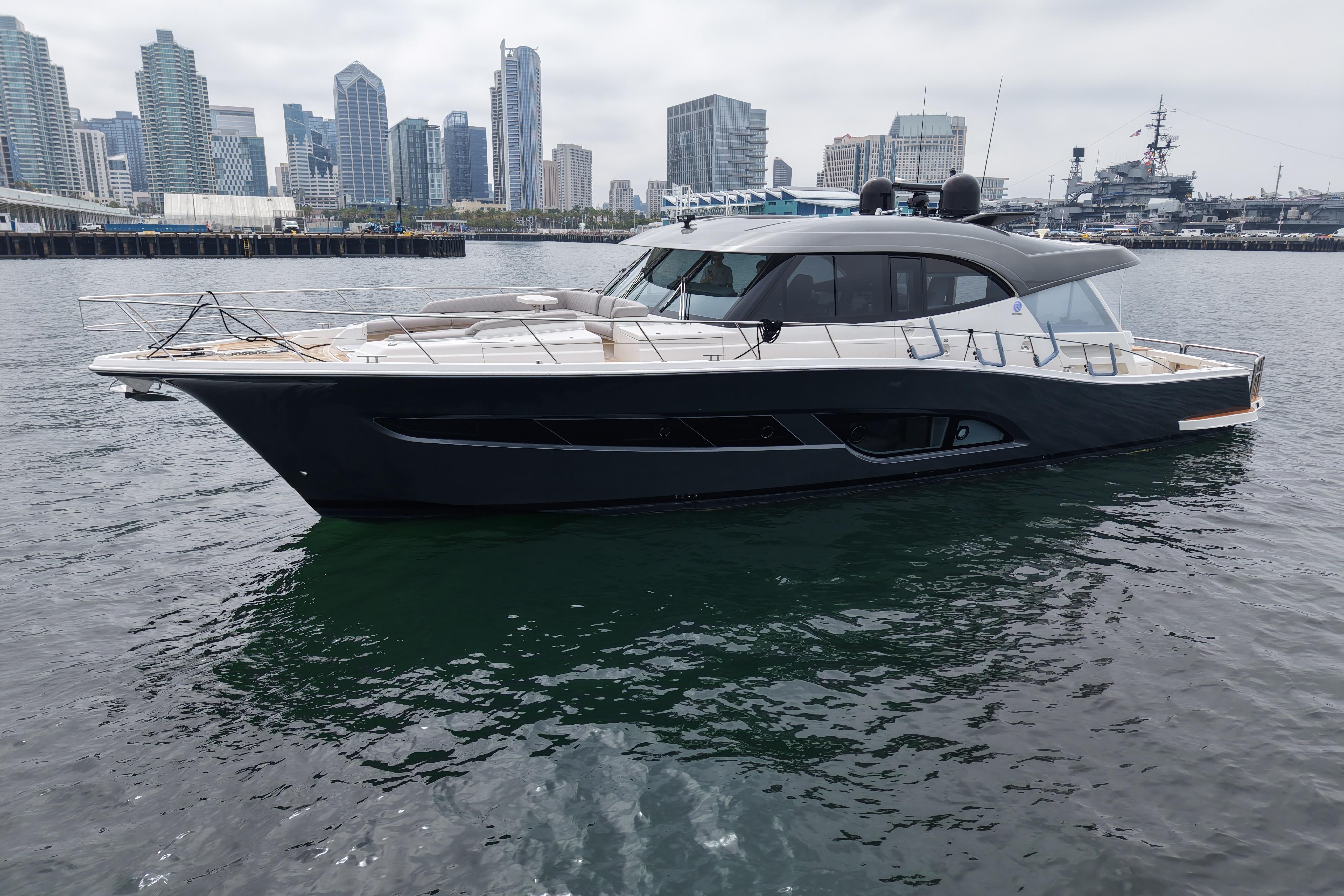 2023 Riviera 645 SUV yacht in urban harbor with city skyline backdrop.