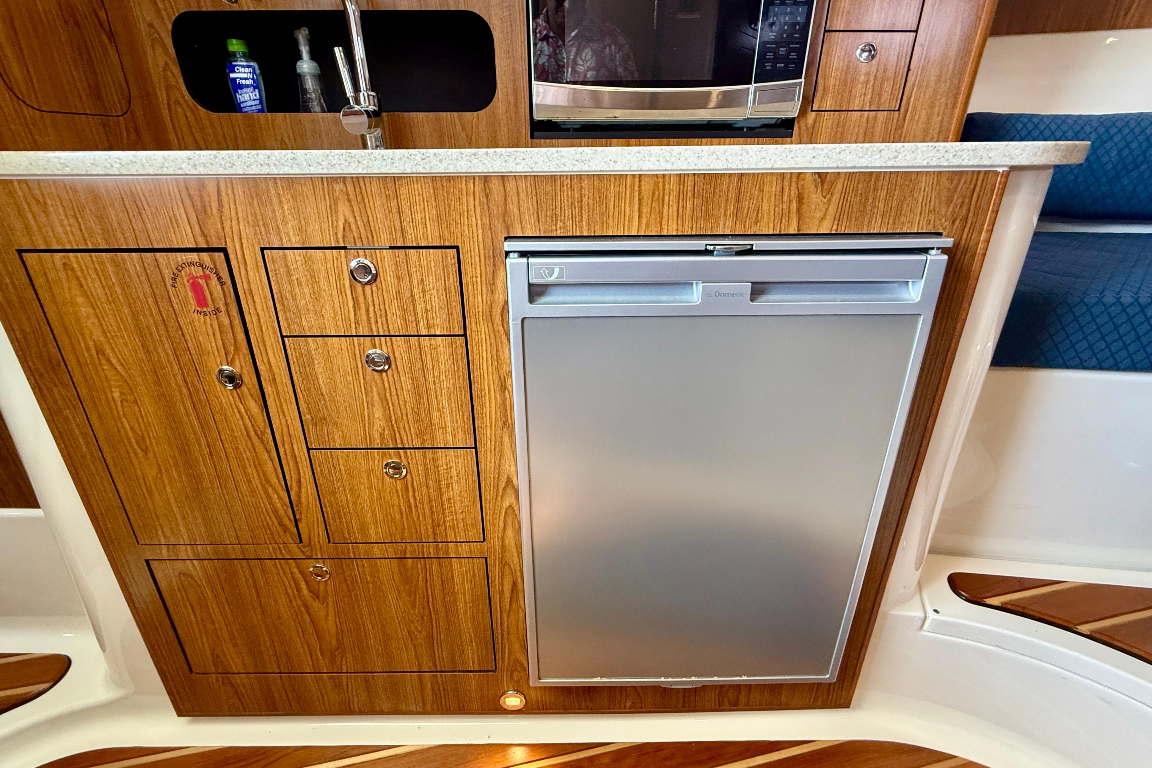 2012 Pursuit OS 345 Offshore boat interior with wooden cabinetry, sink, and compact refrigerator.