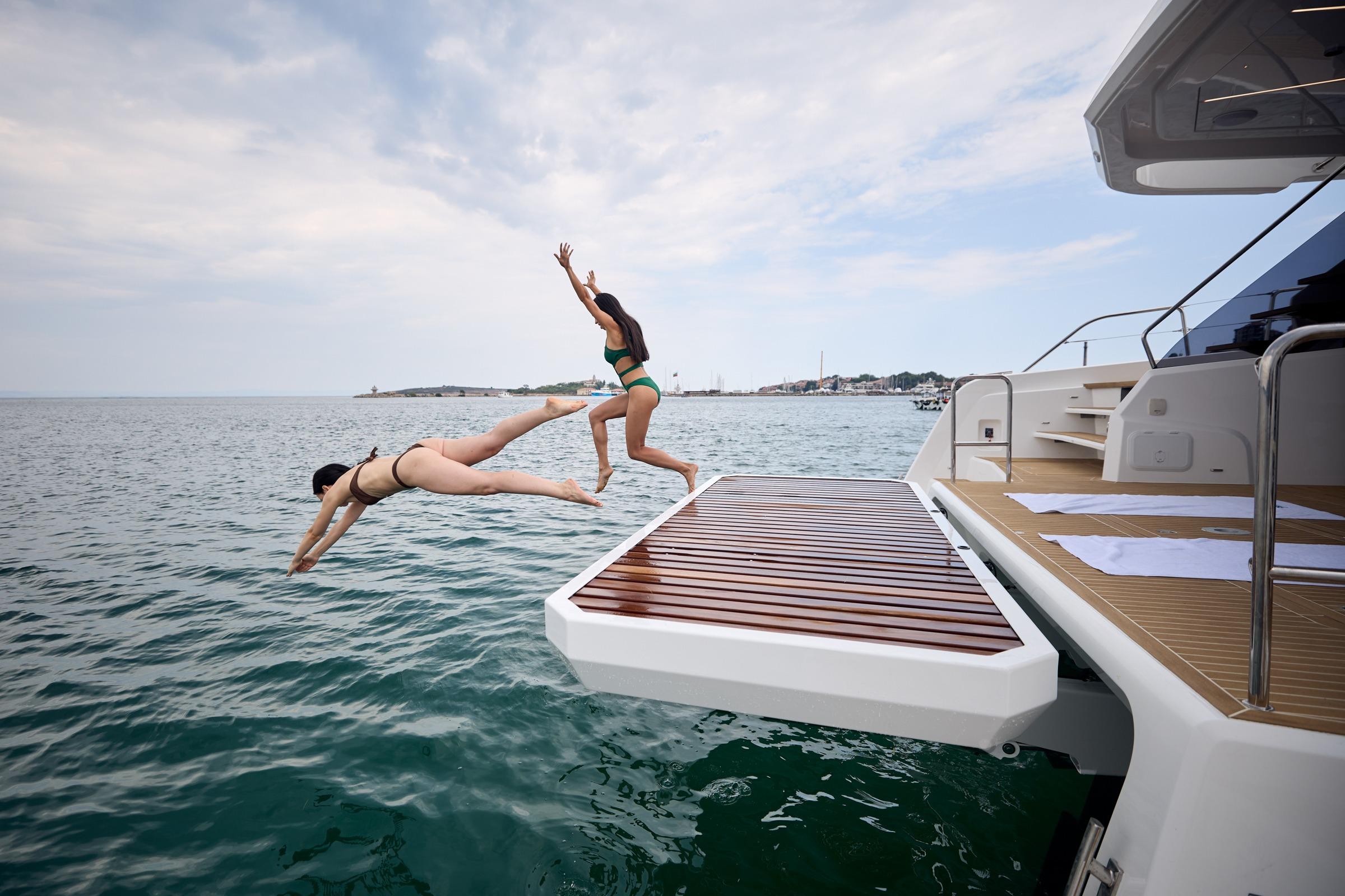 Two people diving off a 2025 Omaya 50 Power Catamaran into the ocean.