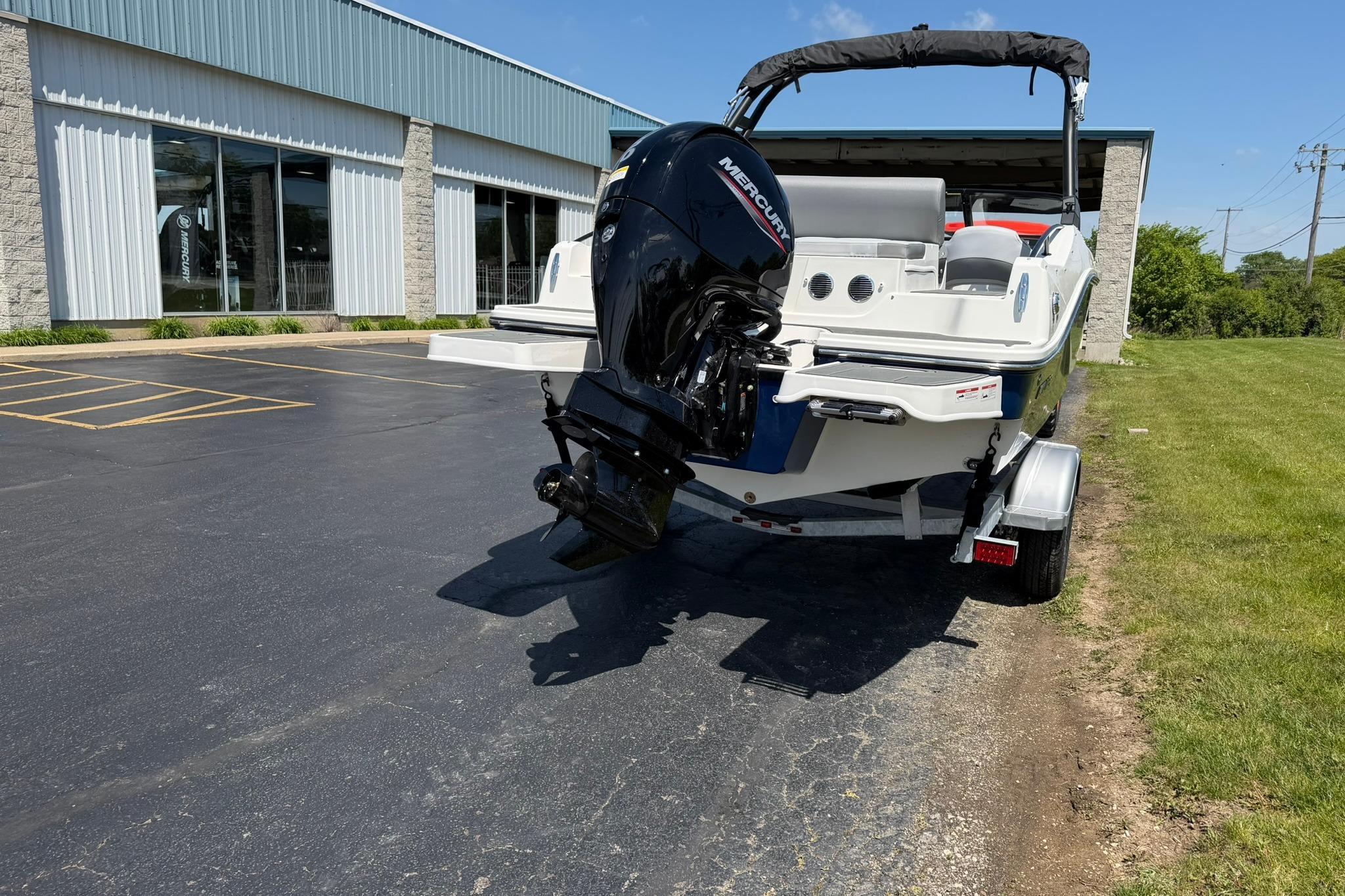 2026 Bayliner D20 boat with Mercury engine on trailer, parked outside a building.