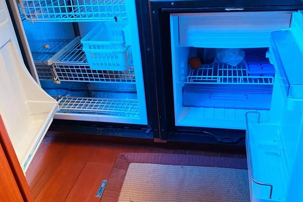 Refrigerator interior on 2012 Hunter Aft Cockpit 50 yacht, featuring wire shelves and blue lighting.