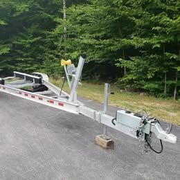 Boat trailer on a paved area with trees in the background.