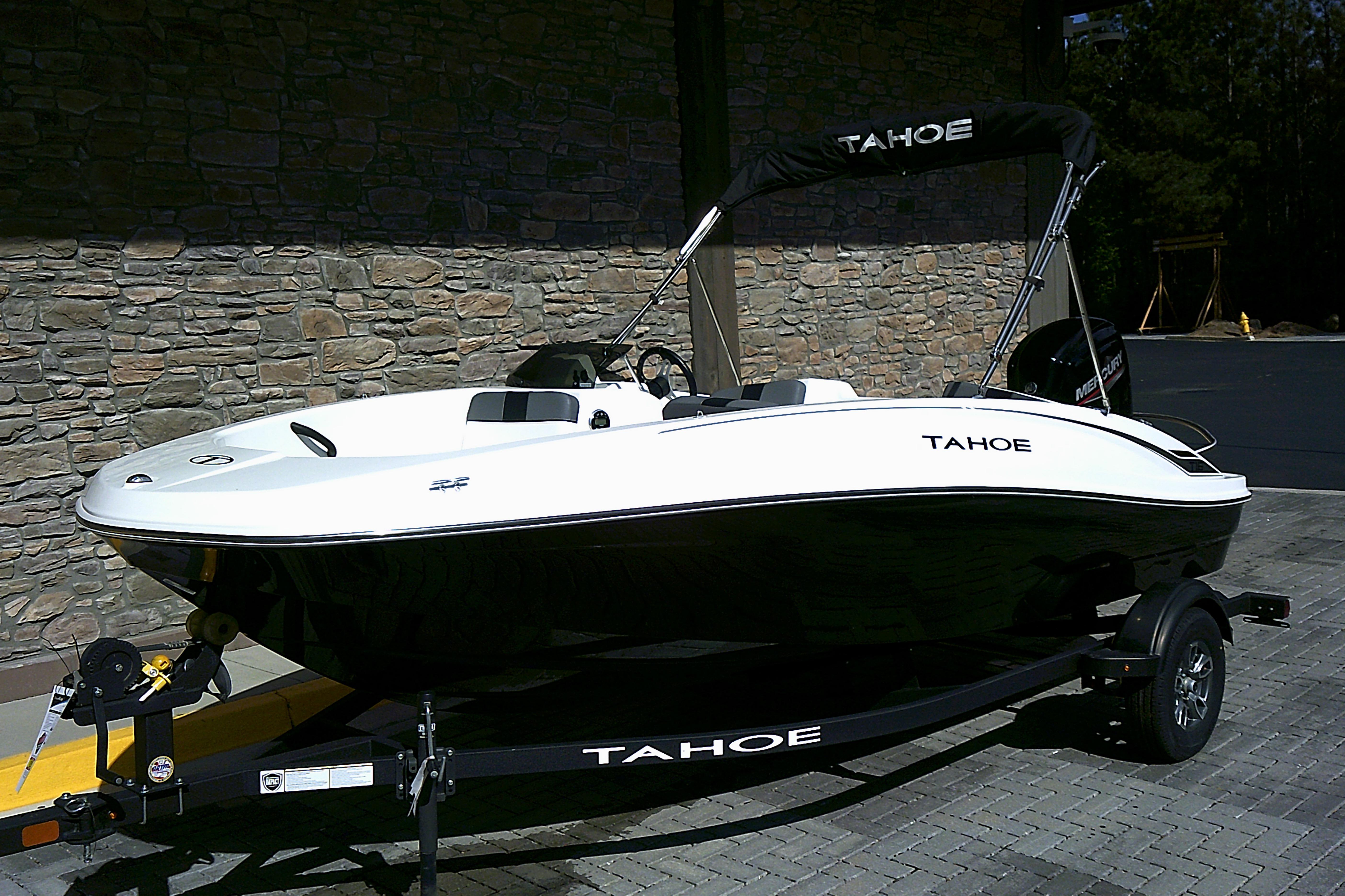 2025 Tahoe T16 boat on trailer, parked by stone wall, featuring sleek design and black accents.