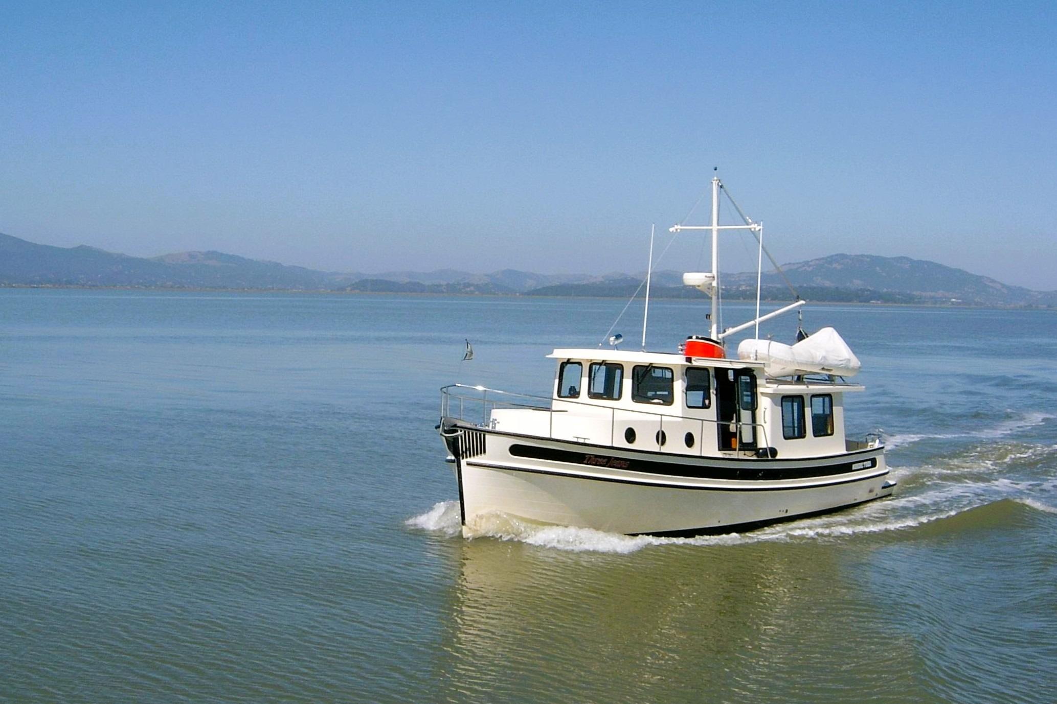 2002 Nordic Tug 37 cruising on calm waters with scenic mountain backdrop.