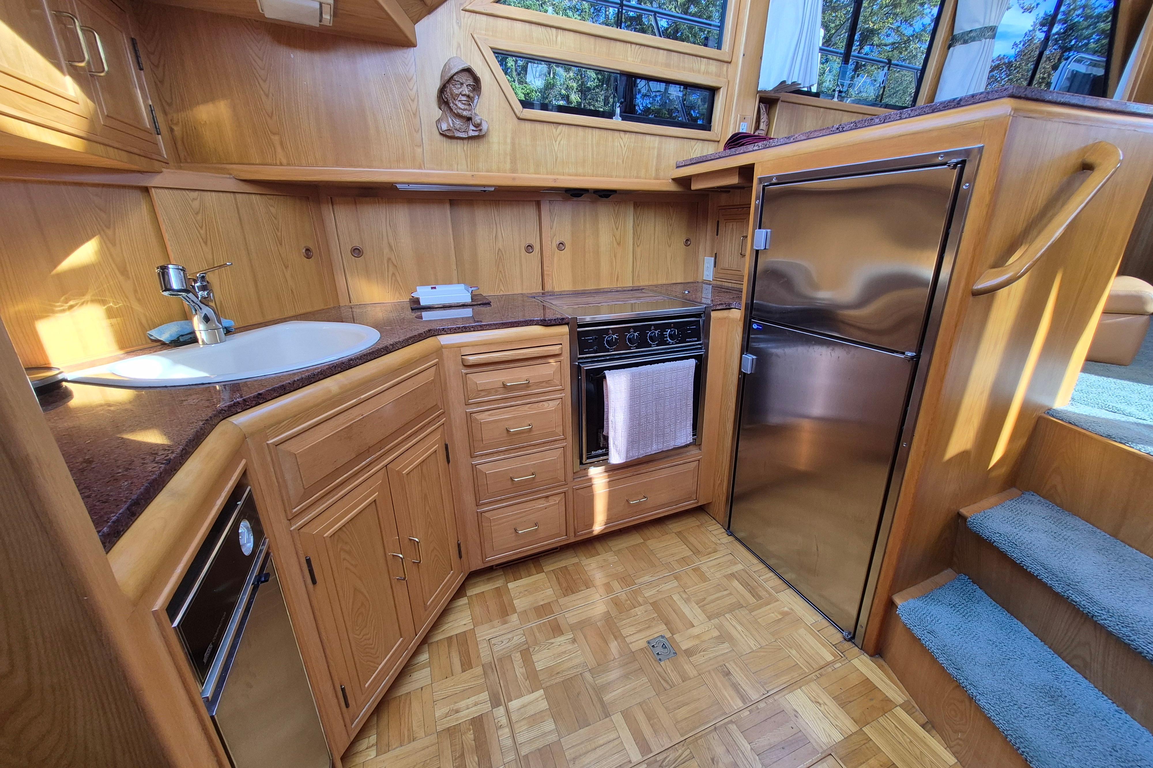 1990 Camargue 48 yacht kitchen with wood cabinetry, stainless steel appliances, and parquet flooring.