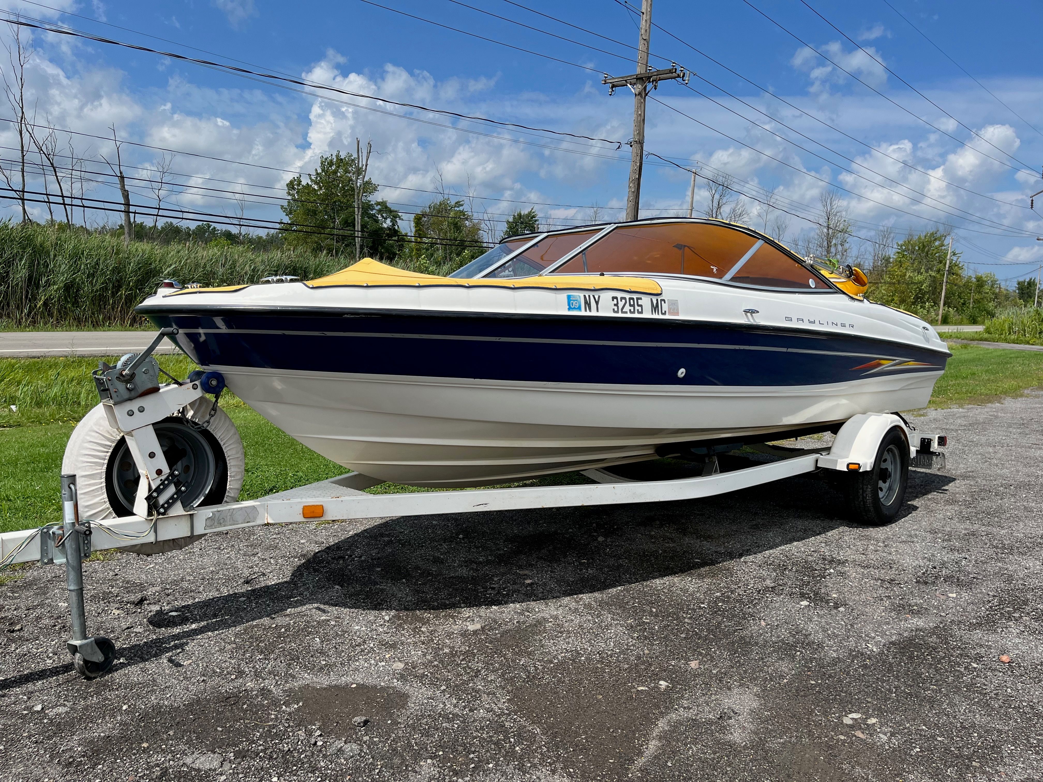 A 2005 Bayliner 205BR on a trailer, parked on a gravel lot beside a road.