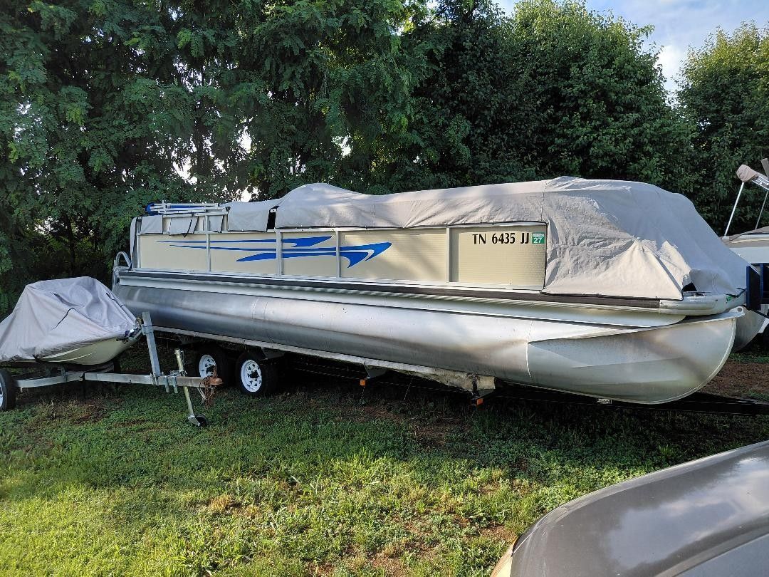 A 1999 Premier 250 Grand Majestic pontoon boat on a trailer, partially covered with a tarp.