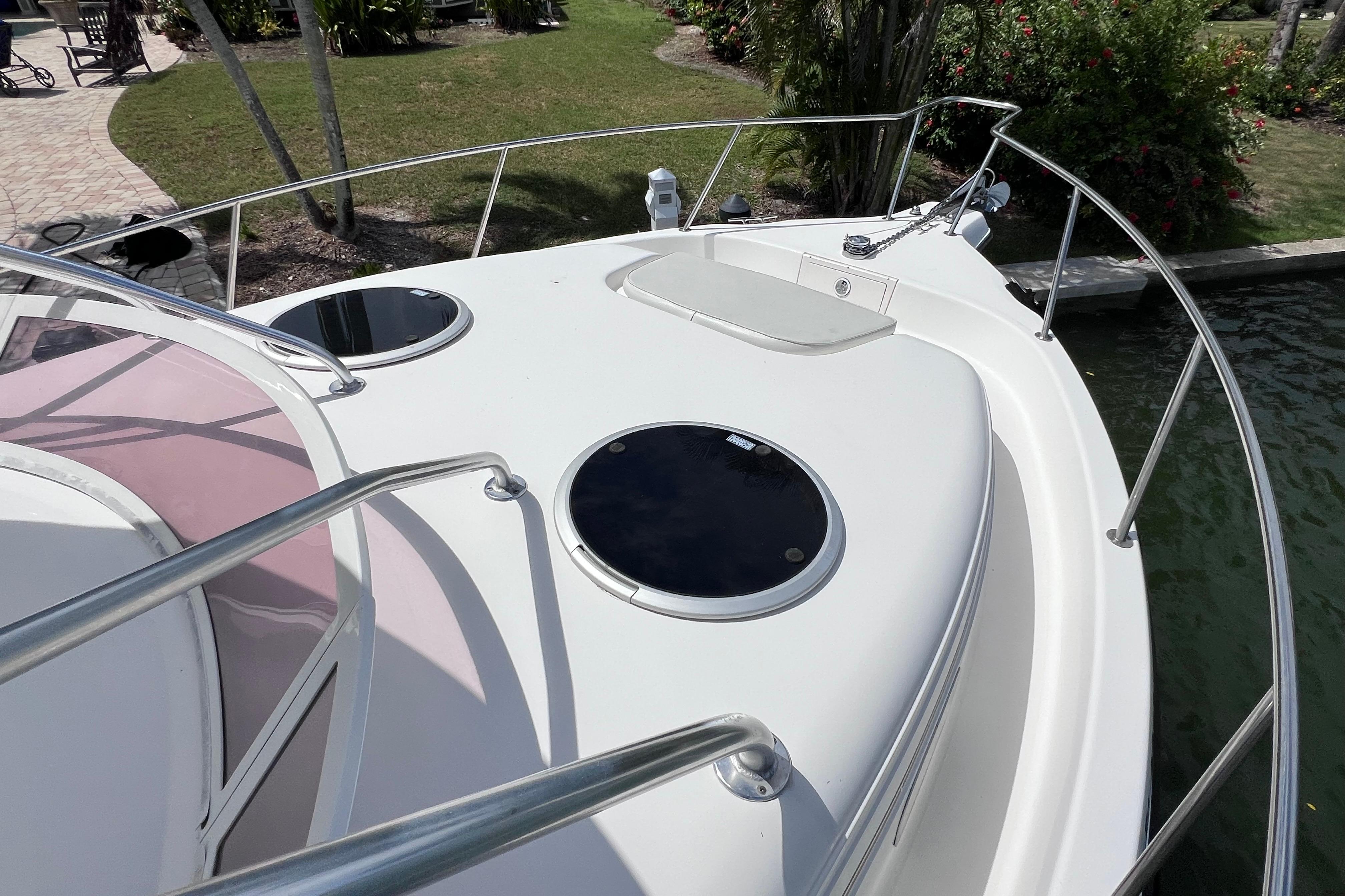 2005 Century 3200 Walk-Around boat deck with hatches and railing, docked near lush greenery.