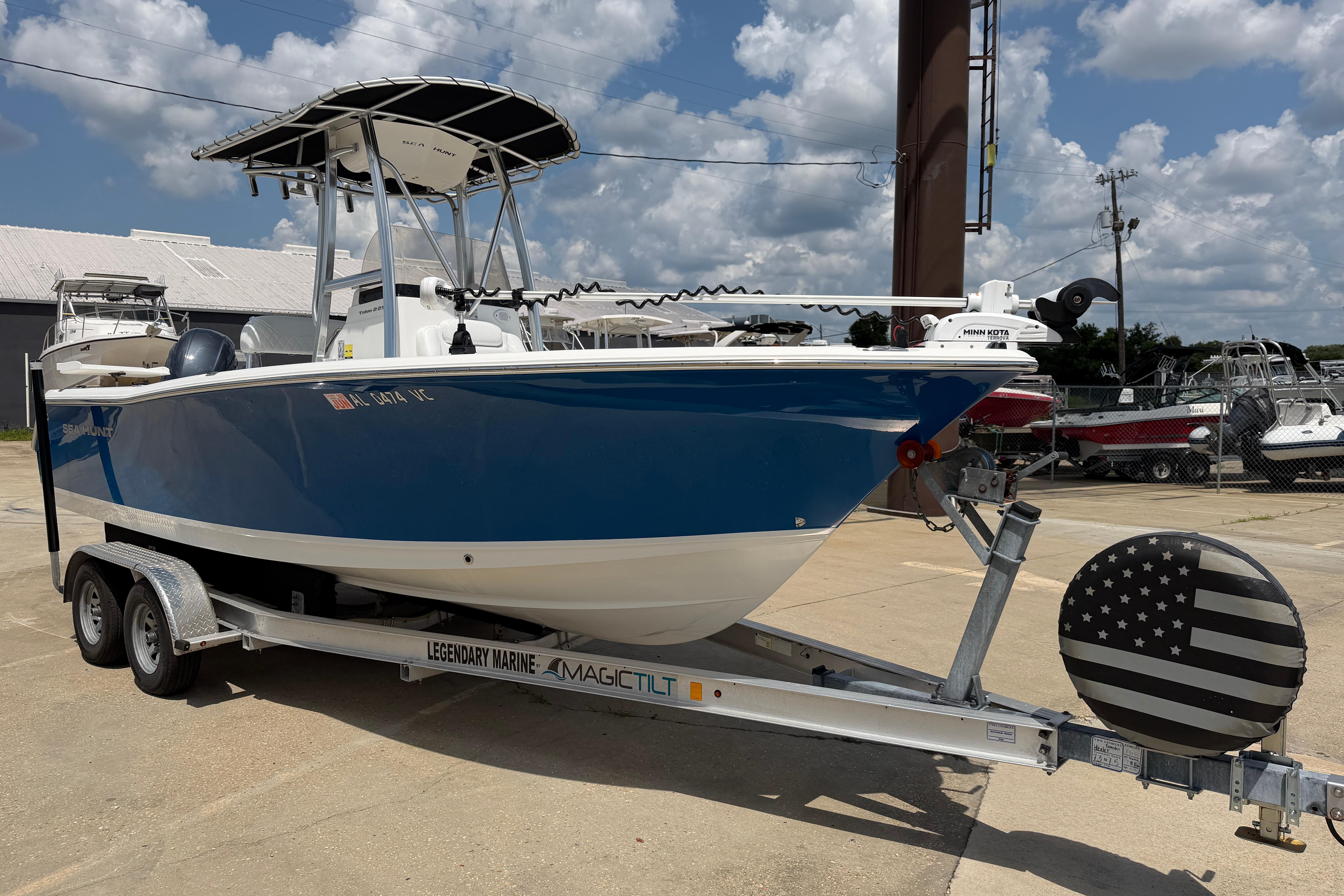 2015 Sea Hunt Triton 225 boat on trailer, blue hull, parked outdoors under cloudy sky.