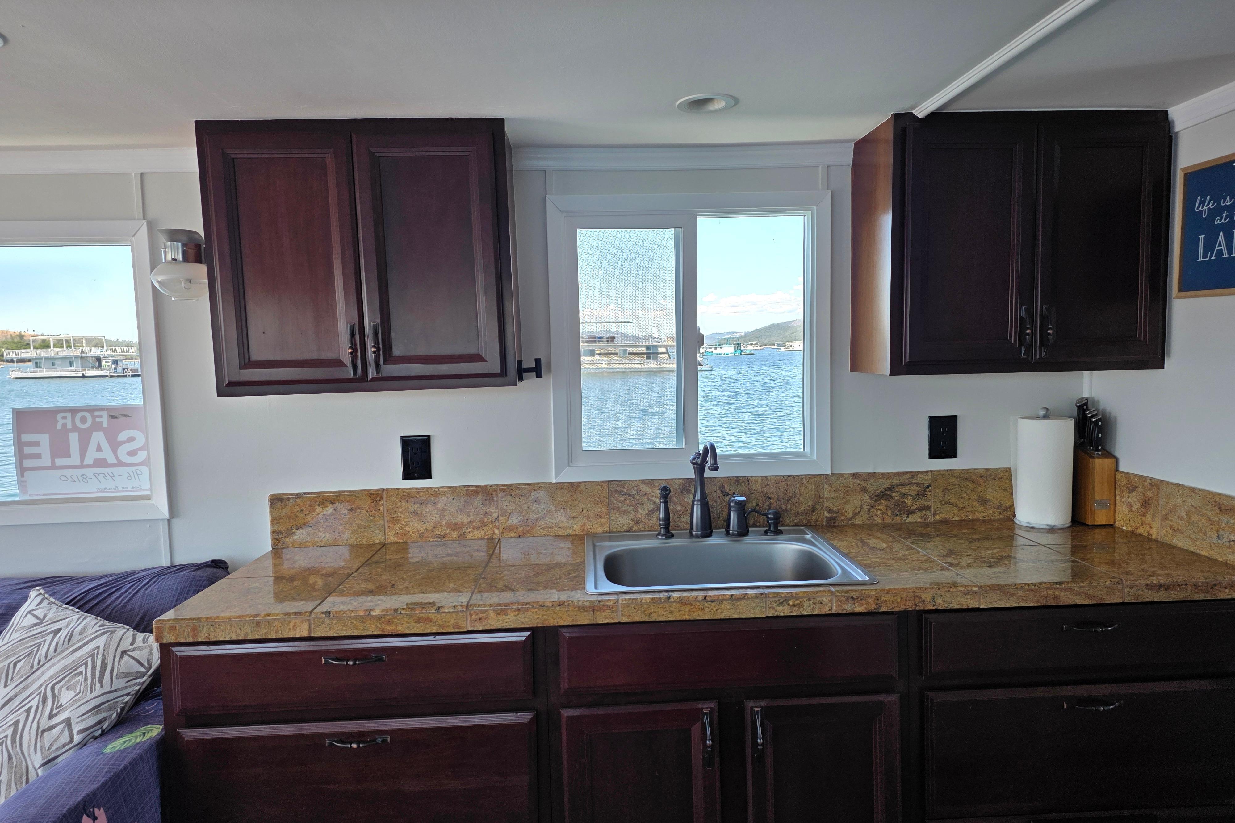 Houseboat kitchen interior with dark cabinets, granite countertops, and a window view of the water.
