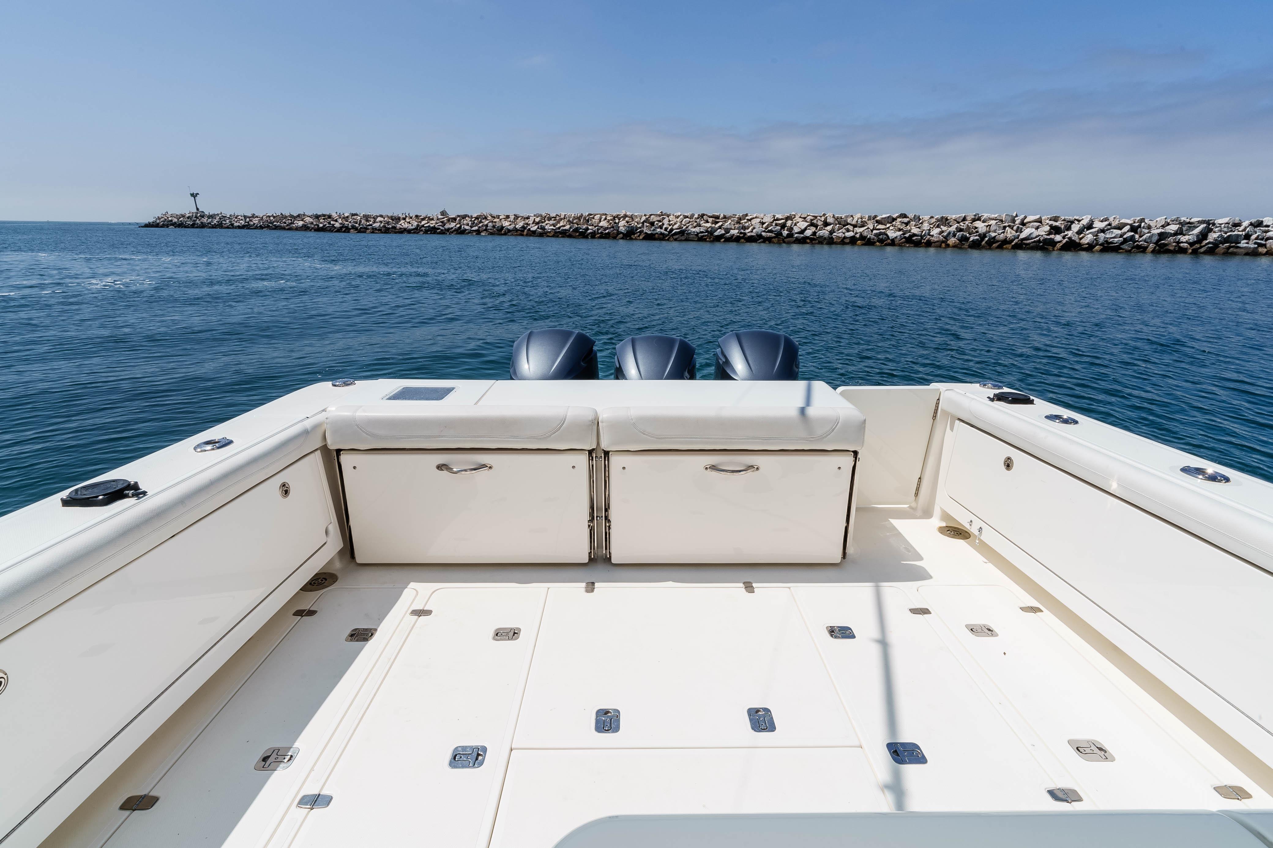 2022 Pursuit OS 385 Offshore boat deck with dual engines, docked near rocky shoreline.