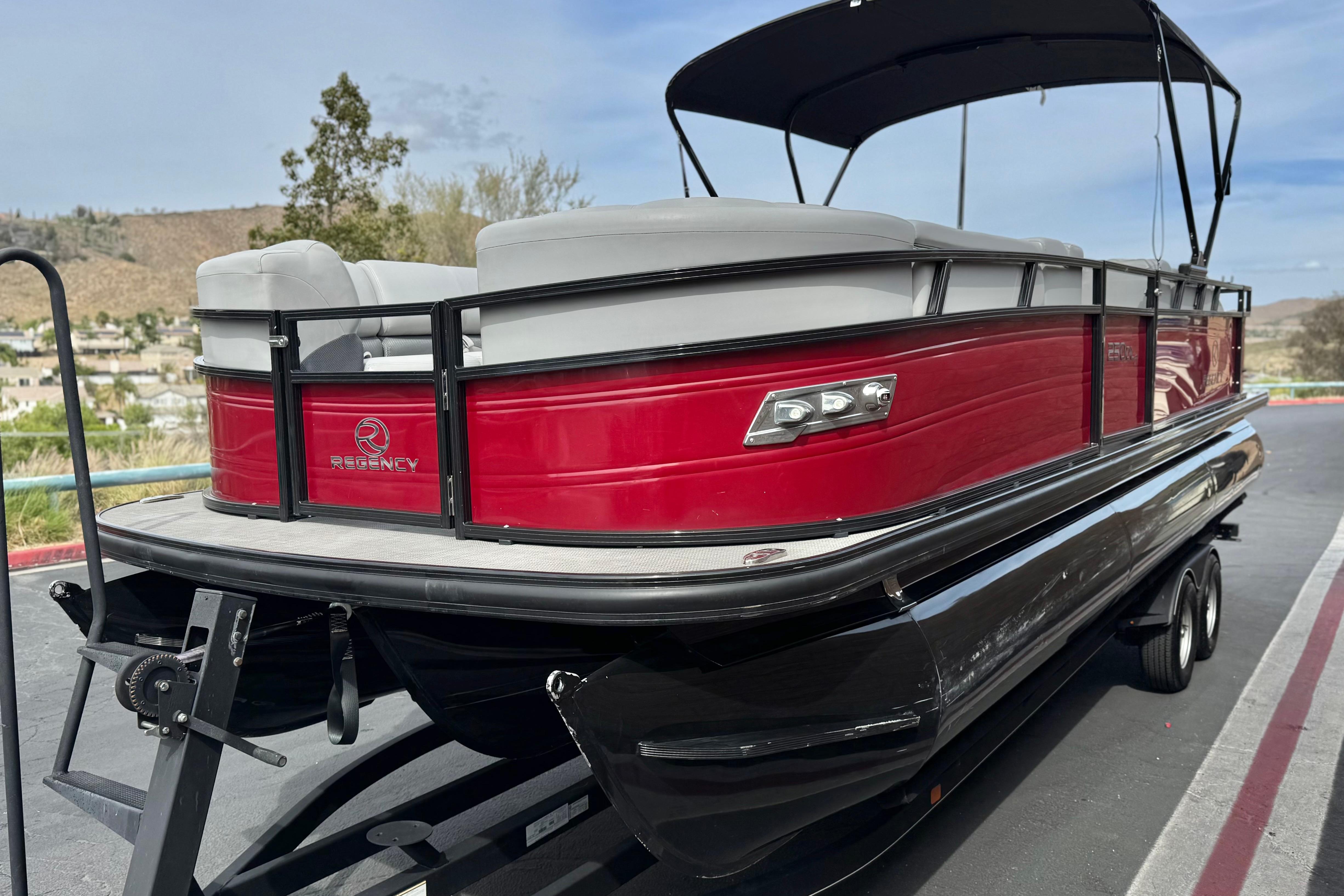2022 Regency 250 DL3 pontoon boat with red exterior and black trailer, parked outdoors.