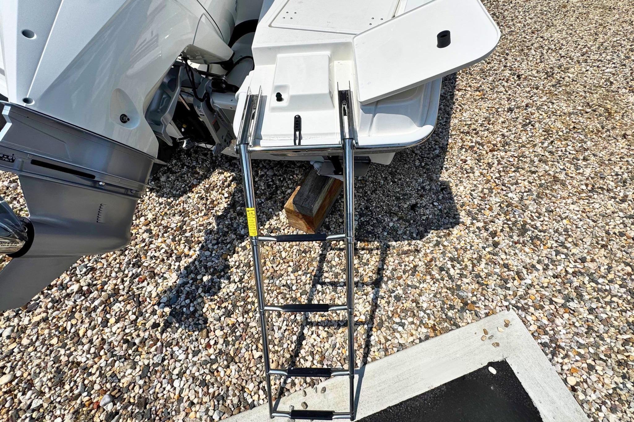 2026 Boston Whaler 220 Dauntless boat with ladder on gravel surface.