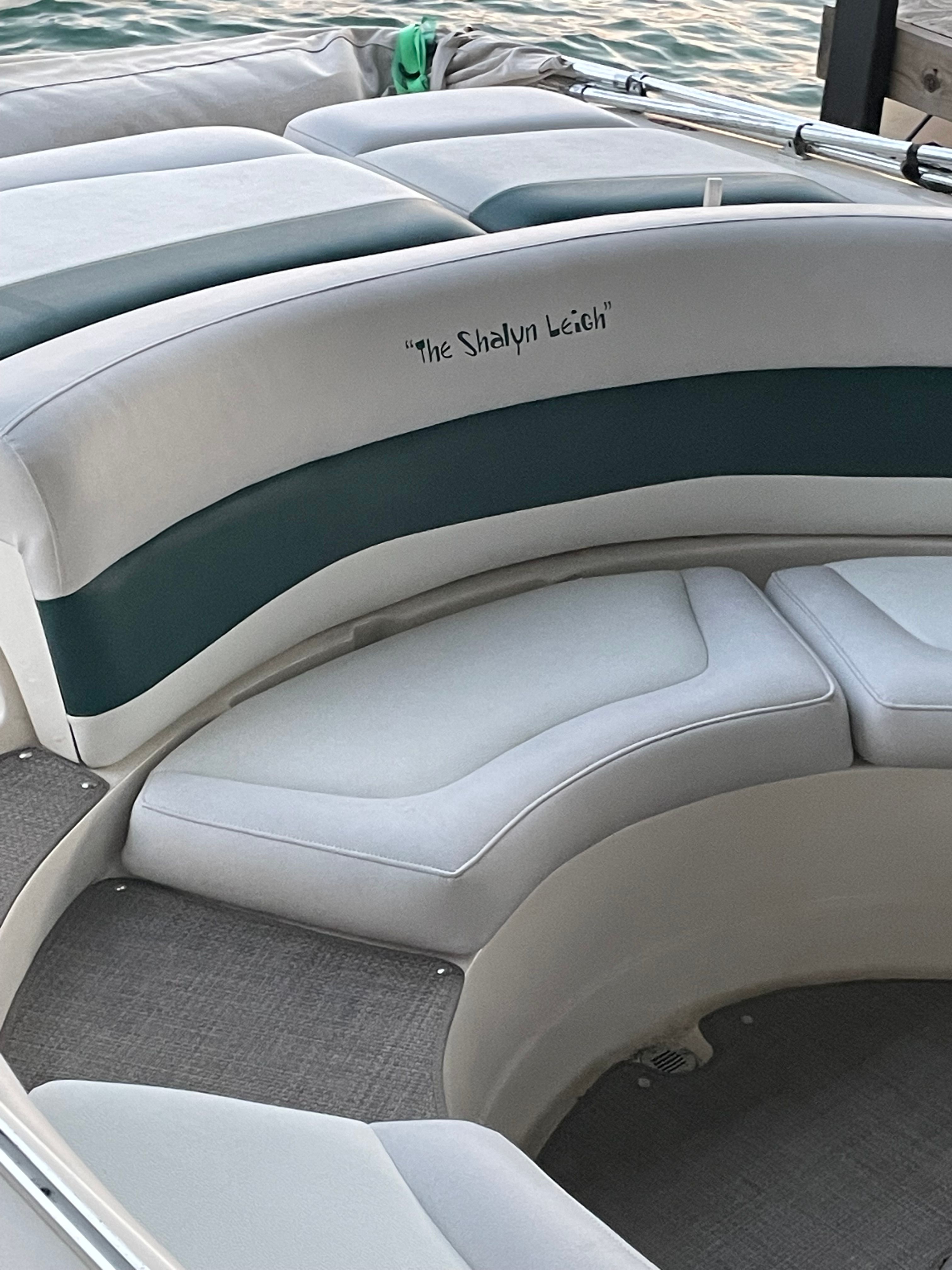 A sleek pontoon boat with gray and green upholstery, resting on calm water.