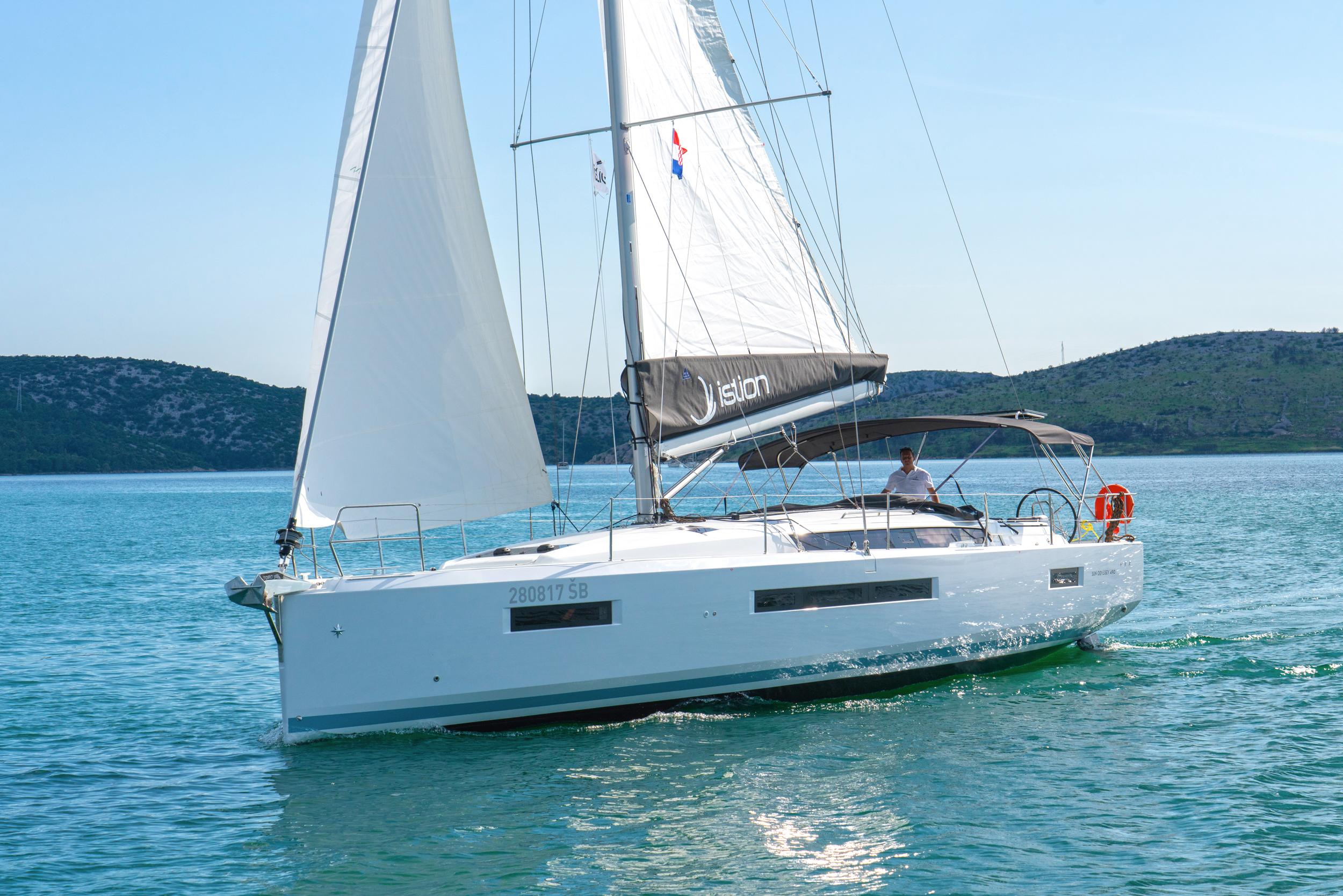 2023 Jeanneau Sun Odyssey 490 sailing on calm waters, showcasing sleek design and white sails.