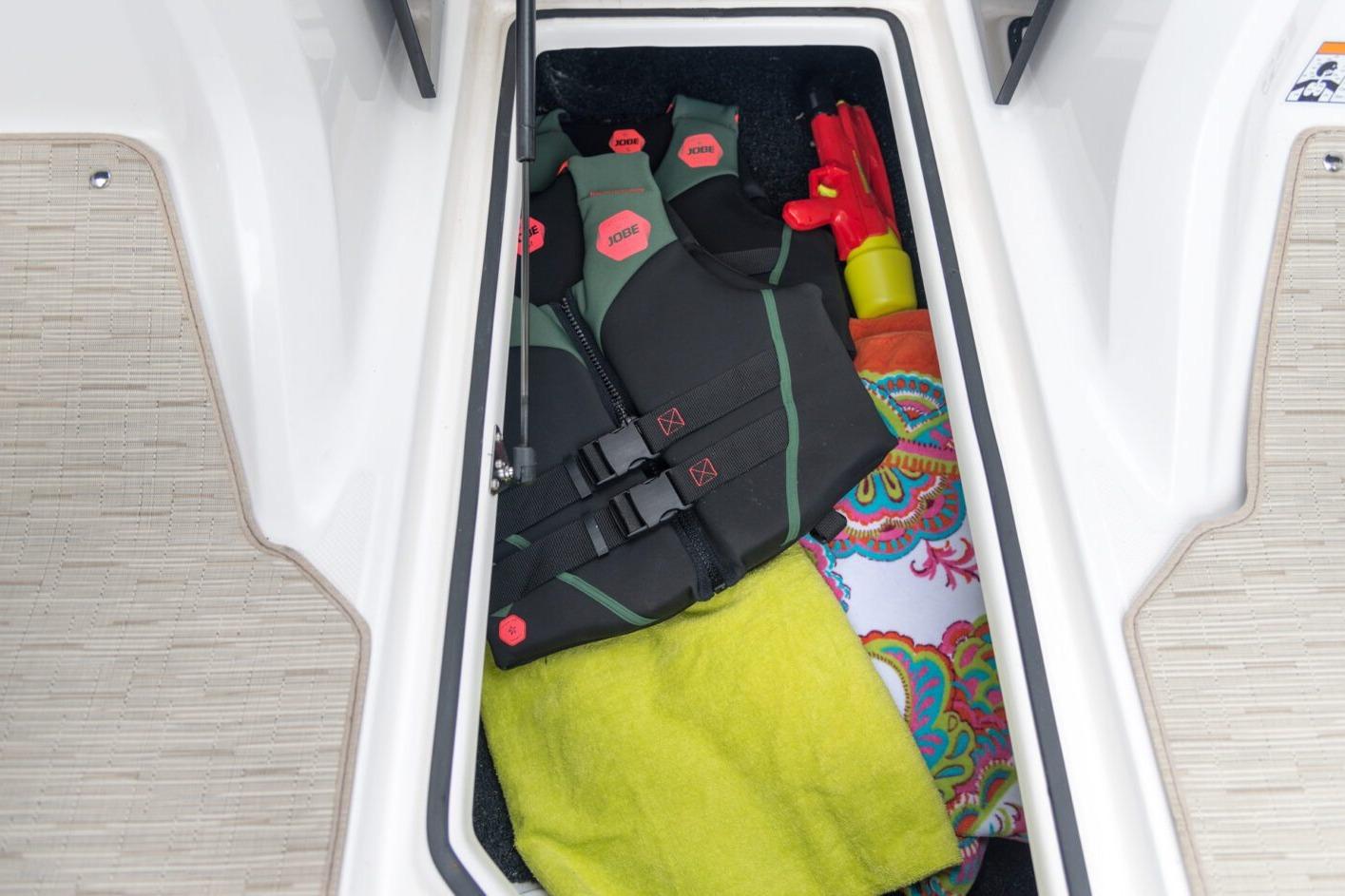 Storage compartment in 2026 Regal 21 OBX boat with life jacket and colorful towels.
