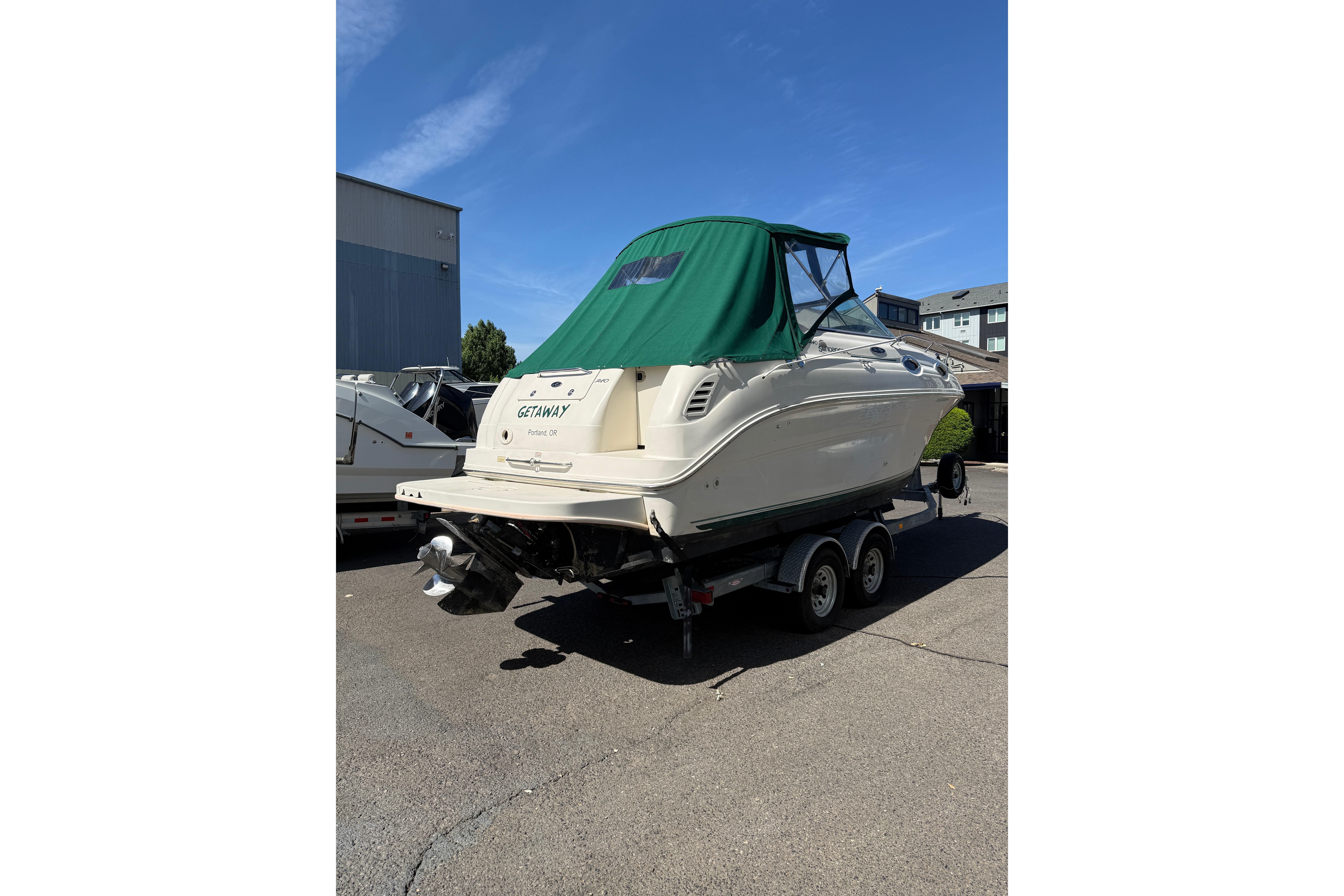 2004 Sea Ray 240 Sundancer boat on trailer with green canopy, parked outdoors.