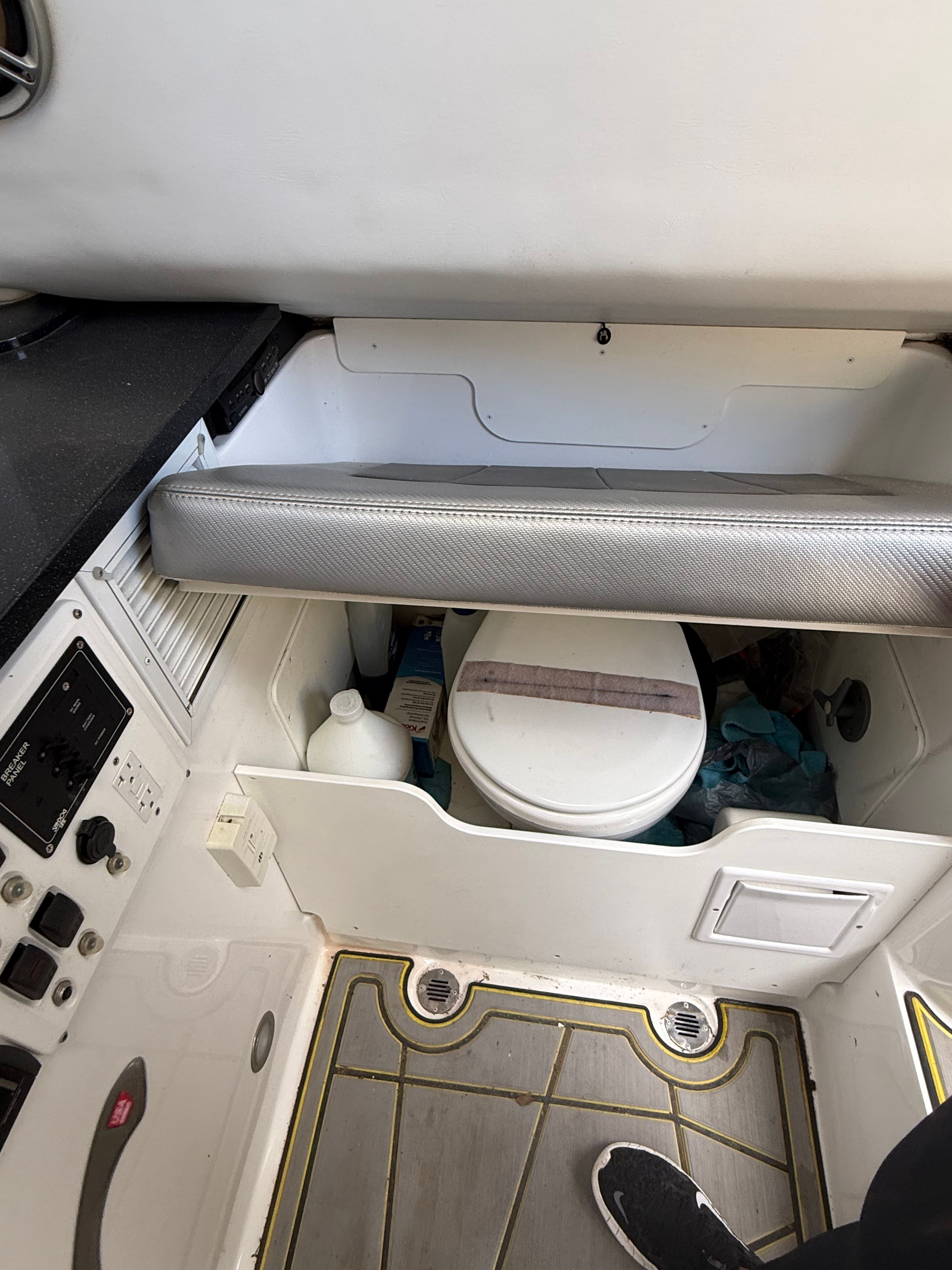 The image shows the interior of a boat with a toilet and a control panel.