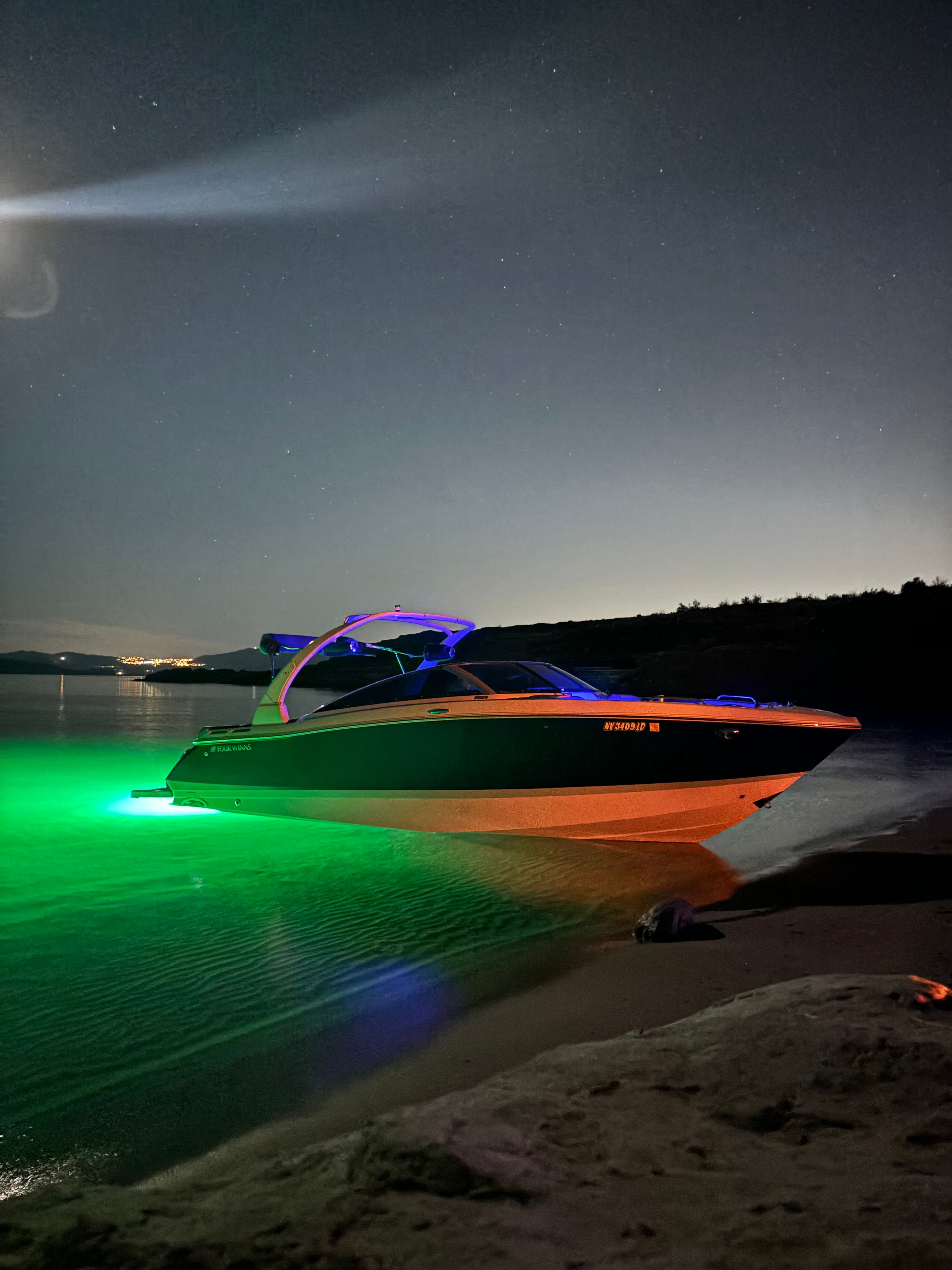 2019 Four Winns H260 boat with green underwater lights at night.